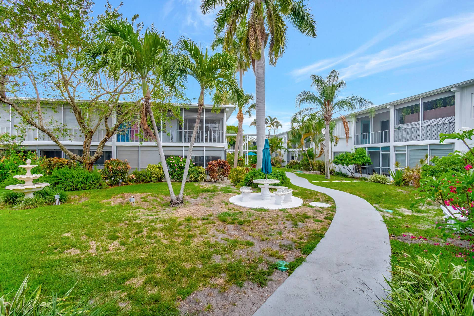 2161 NE 42nd Court, #116, Lighthouse Point, FL 33064 Lush landscaping featuring mature palm trees, a tiered fountain, and a meandering paver pathway