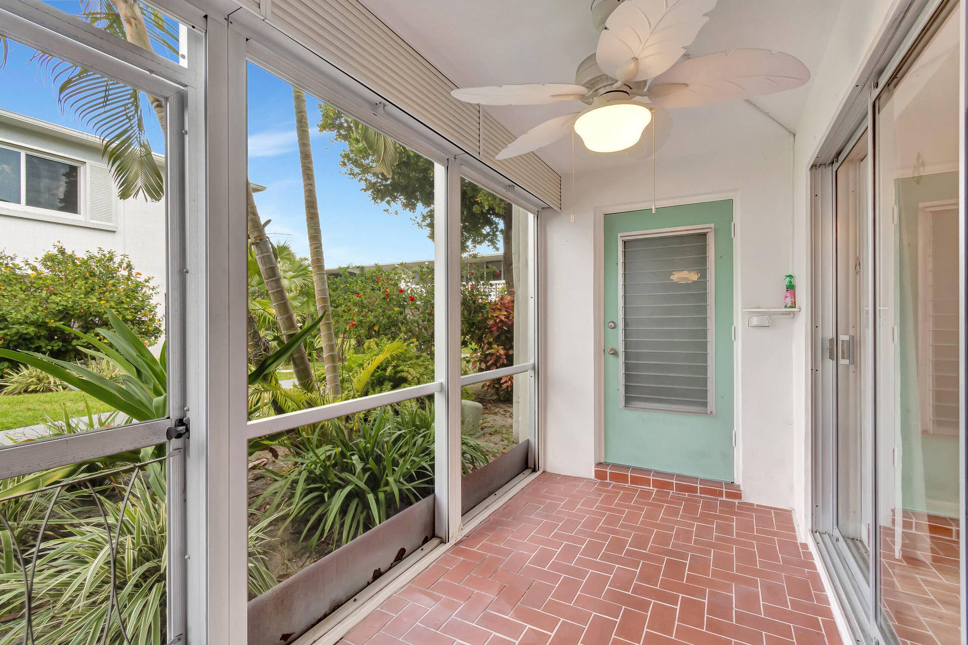 2161 NE 42nd Court, #116, Lighthouse Point, FL 33064 Screened patio featuring herringbone-patterned brick-finish flooring, a ceiling fan with integrated lighting, and a paneled door