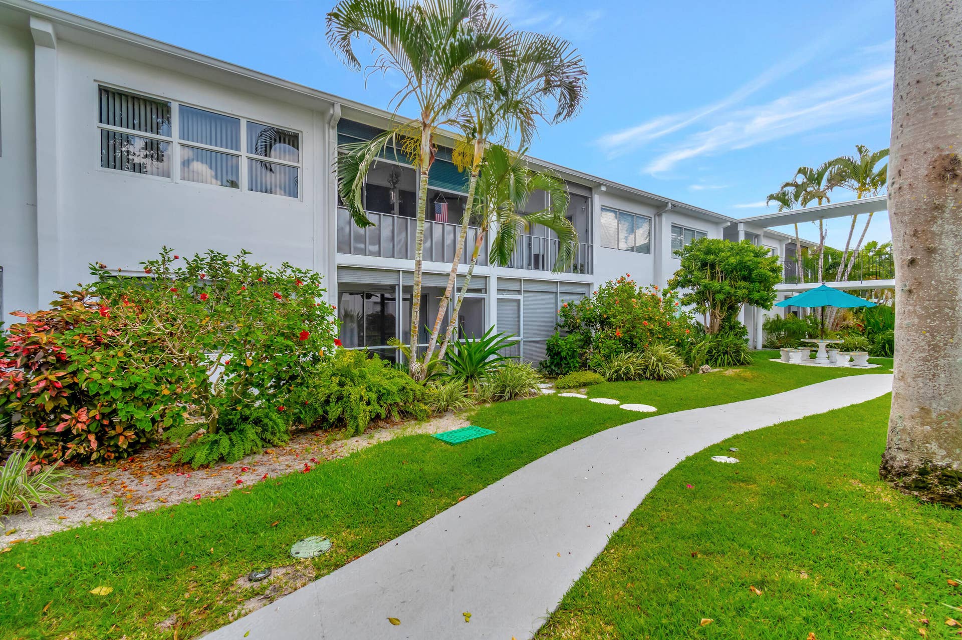 2161 NE 42nd Court, #116, Lighthouse Point, FL 33064 Manicured grounds featuring a winding pathway, lush landscaping, mature palm trees, and a shaded outdoor seating area
