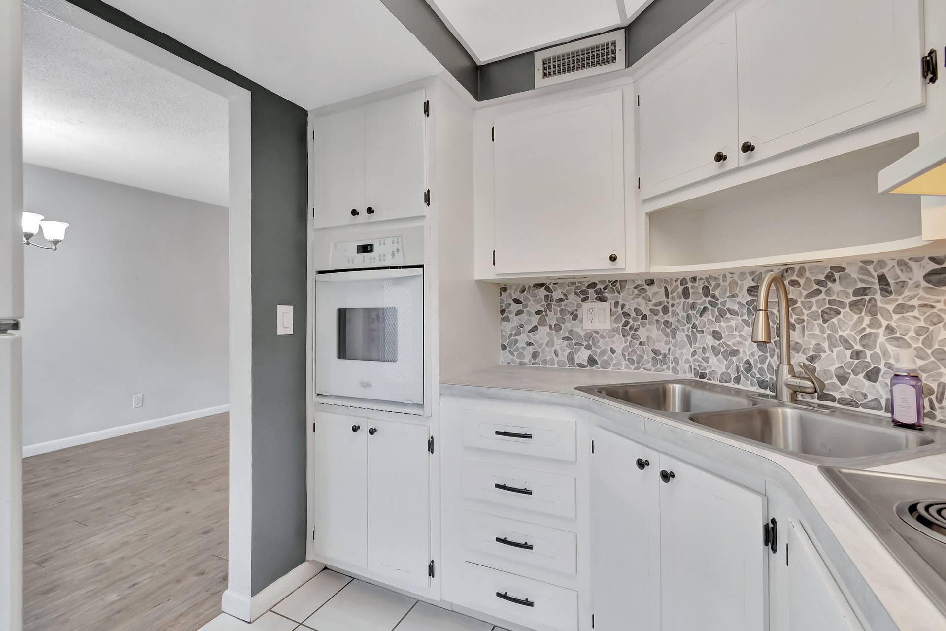 2161 NE 42nd Court, #116, Lighthouse Point, FL 33064 White cabinetry, pebble tile backsplash, dual basin stainless steel sink, built-in oven, and wood-finish flooring