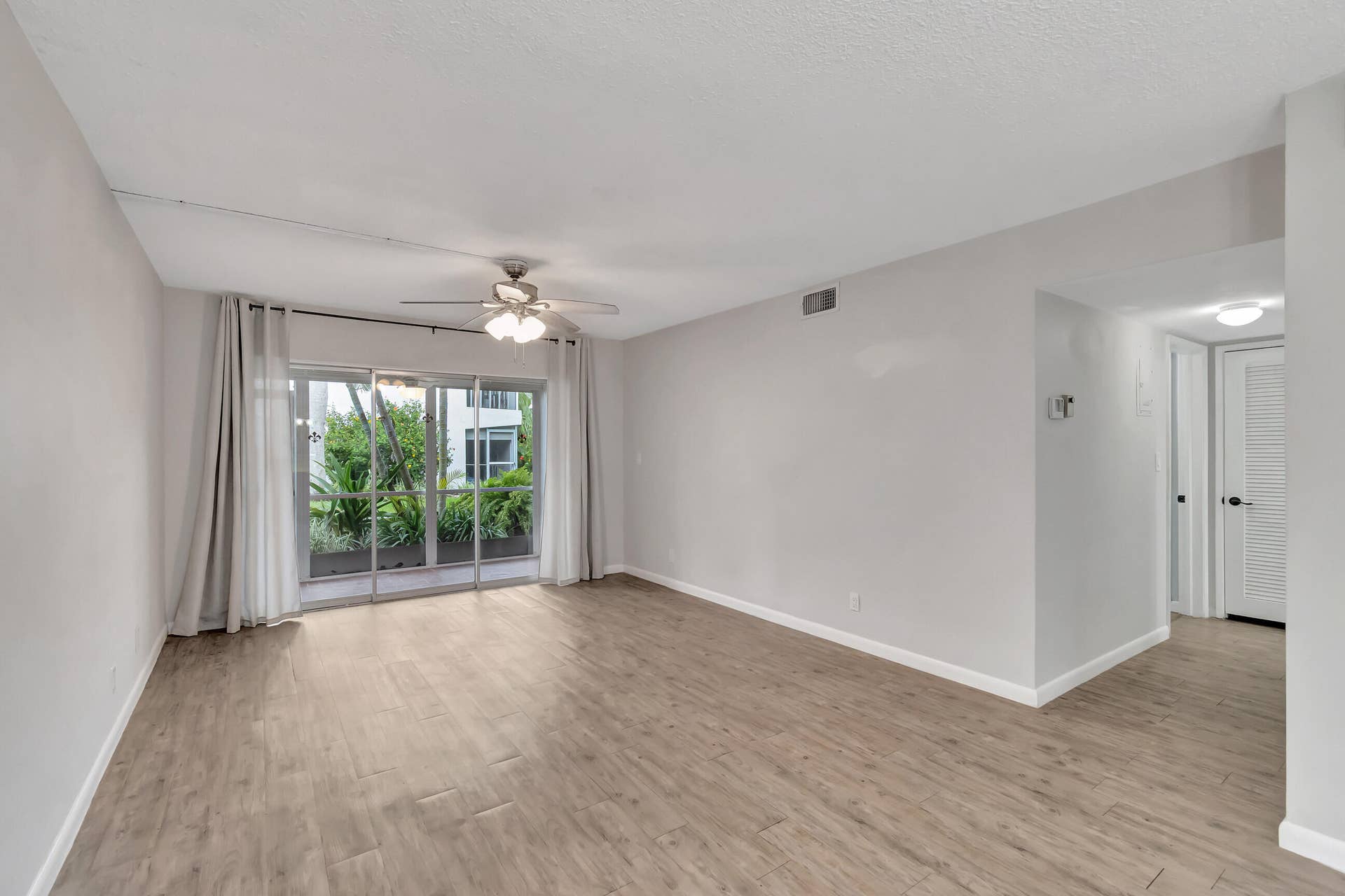 2161 NE 42nd Court, #116, Lighthouse Point, FL 33064 Wood-finish flooring throughout, sliding glass doors to outdoor space, ceiling fan with integrated lighting, and neutral wall color