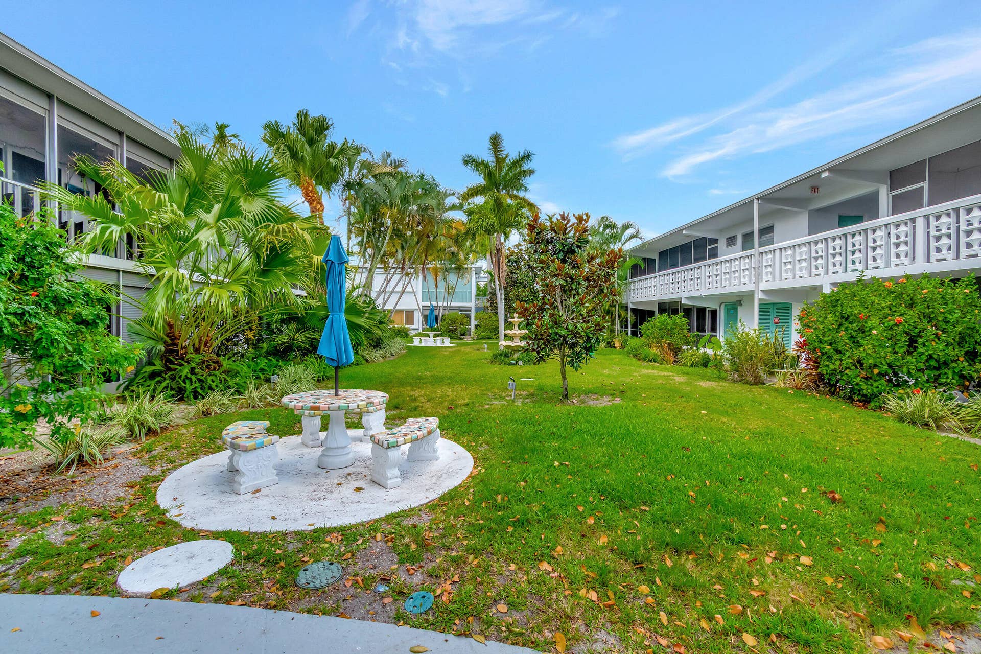 2161 NE 42nd Court, #116, Lighthouse Point, FL 33064 Expansive lawn area featuring a stone patio with seating, mature palm trees, diverse landscaping, and a decorative fountain