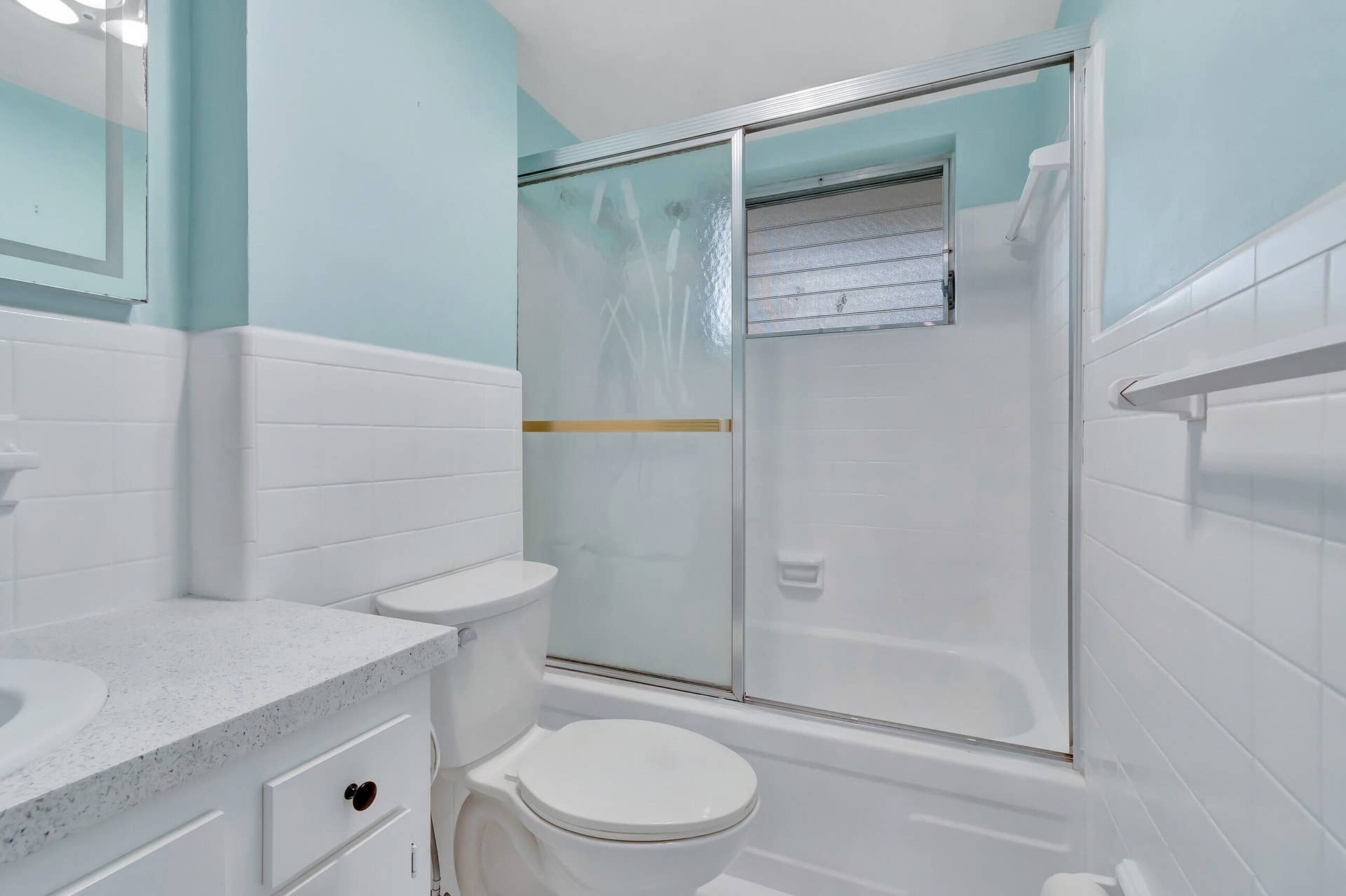 2161 NE 42nd Court, #116, Lighthouse Point, FL 33064 Bathroom featuring a bathtub with sliding glass doors, a window, a white vanity with an integrated sink, and white wall tiling