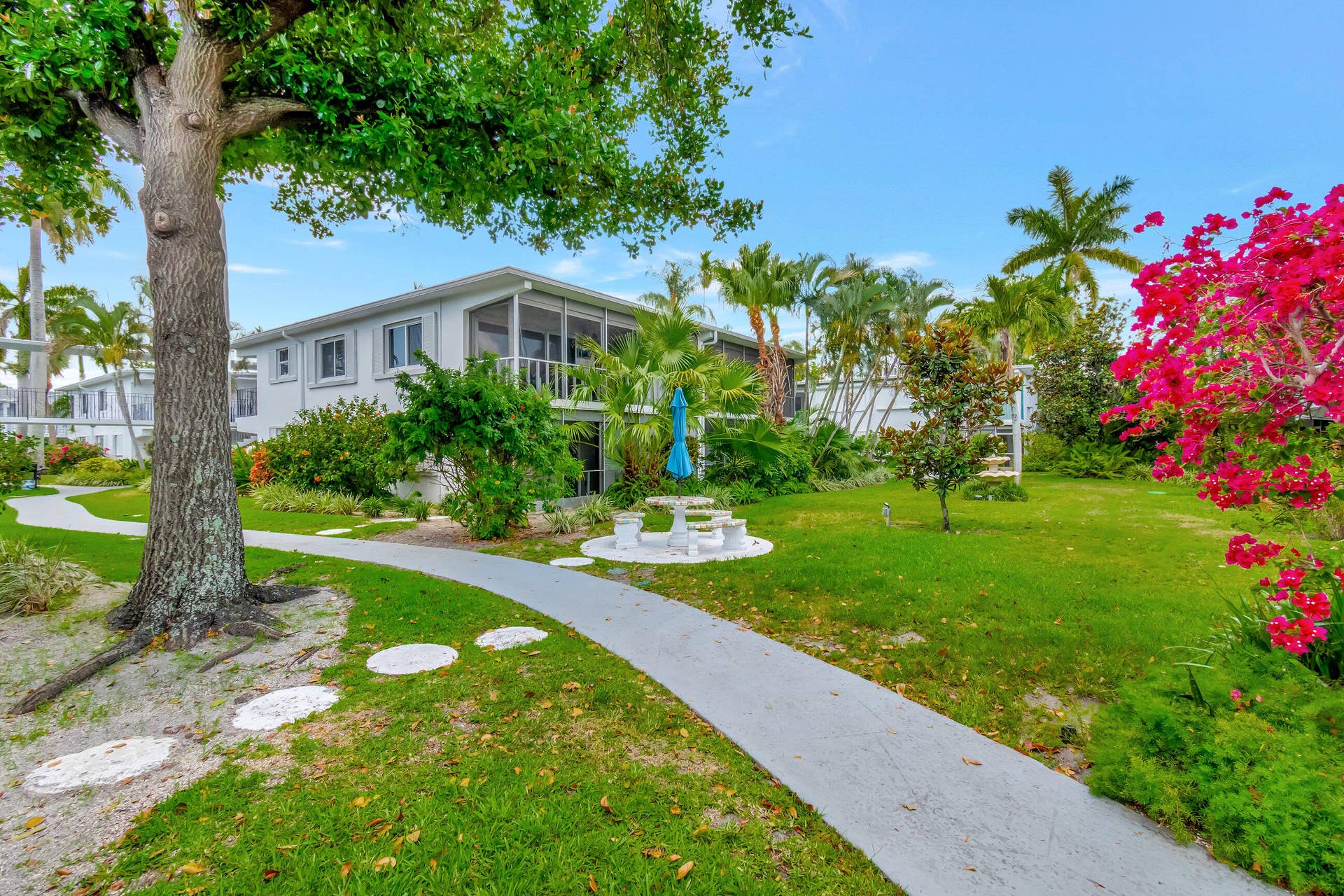 2161 NE 42nd Court, #116, Lighthouse Point, FL 33064 Expansive green space featuring a concrete pathway, established trees, and vibrant bougainvillea