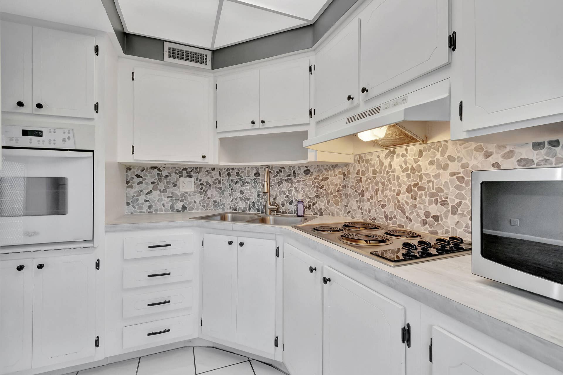 2161 NE 42nd Court, #116, Lighthouse Point, FL 33064 Kitchen featuring white cabinetry, pebble tile backsplash, built-in wall oven, and a cooktop