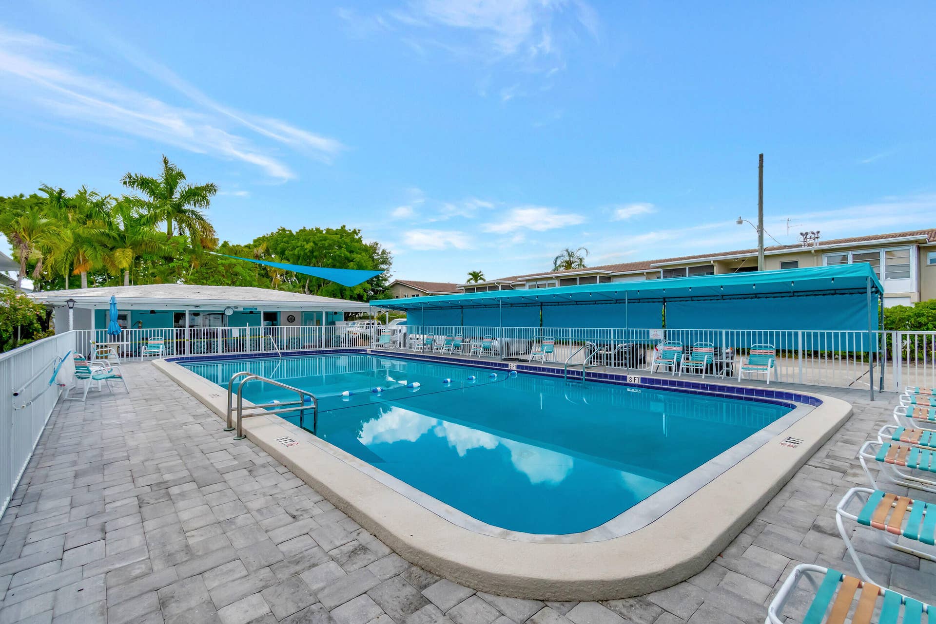 2161 NE 42nd Court, #116, Lighthouse Point, FL 33064 Rectangular swimming pool with integrated steps, surrounded by paver patio surfacing, a poolside building, and a shaded outdoor area