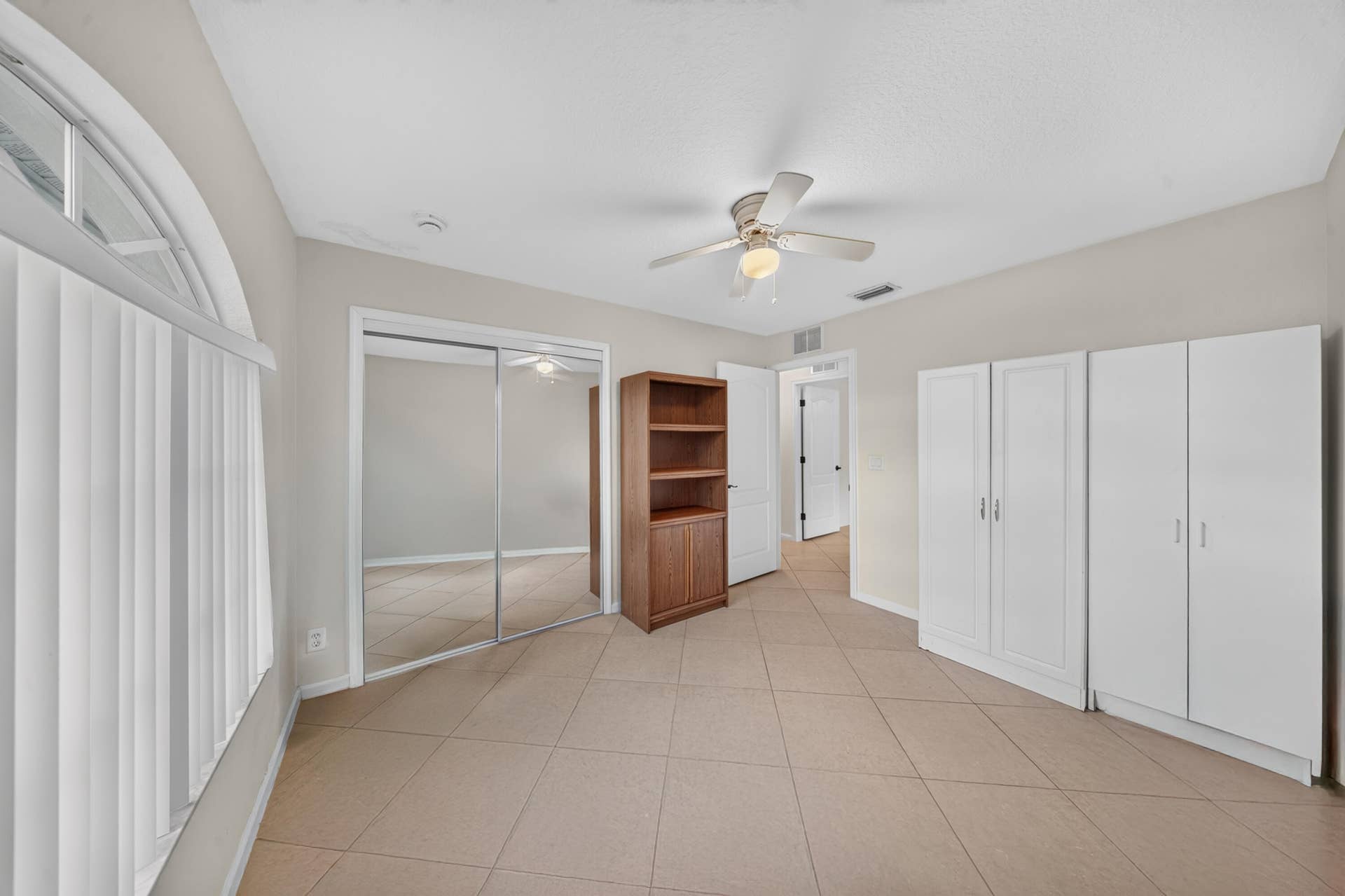 3274 SW CRUMPACKER Street, Port St Lucie, FL 34953 Tiled flooring, overhead ceiling fan, mirrored closet doors, built-in white cabinetry, and an arched window with vertical blinds
