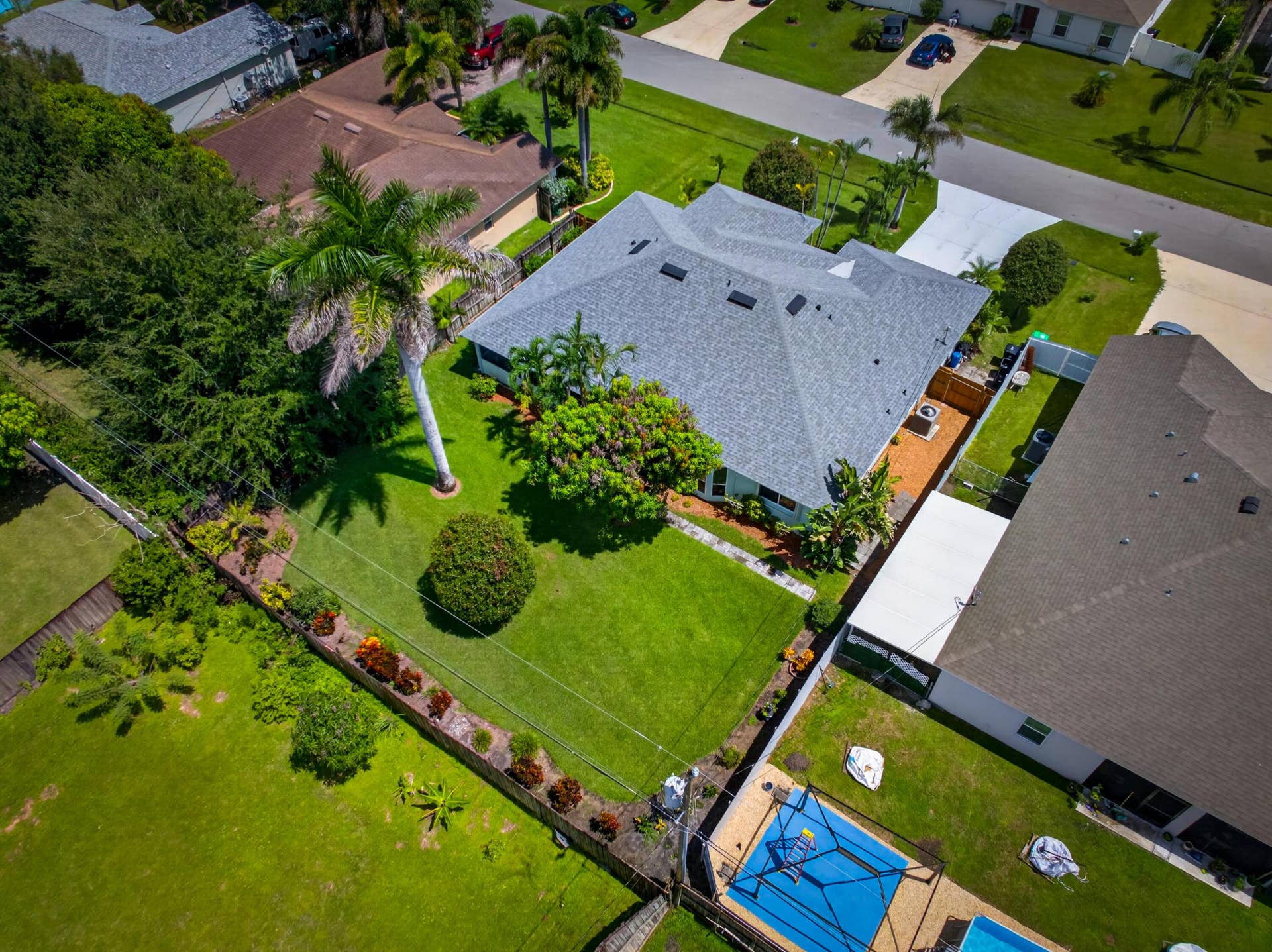 3274 SW CRUMPACKER Street, Port St Lucie, FL 34953 Single-story residence with a gray shingle roof, expansive green lawn, mature palm trees, landscaped garden beds, and a paved driveway