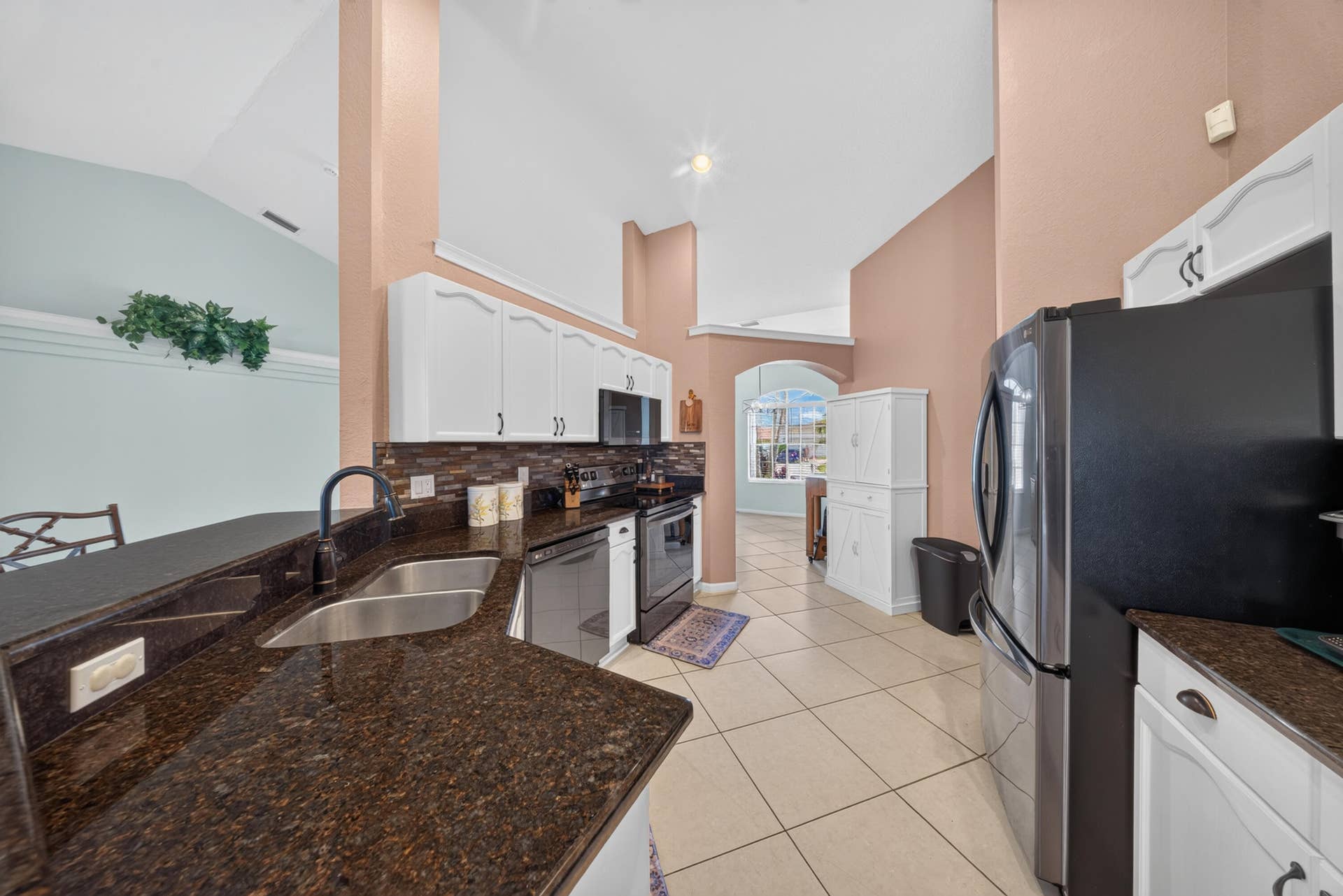 3274 SW CRUMPACKER Street, Port St Lucie, FL 34953 Kitchen featuring vaulted ceilings, white cabinetry with crown molding, dark stone countertops, stainless steel appliances, and a tile backsplash