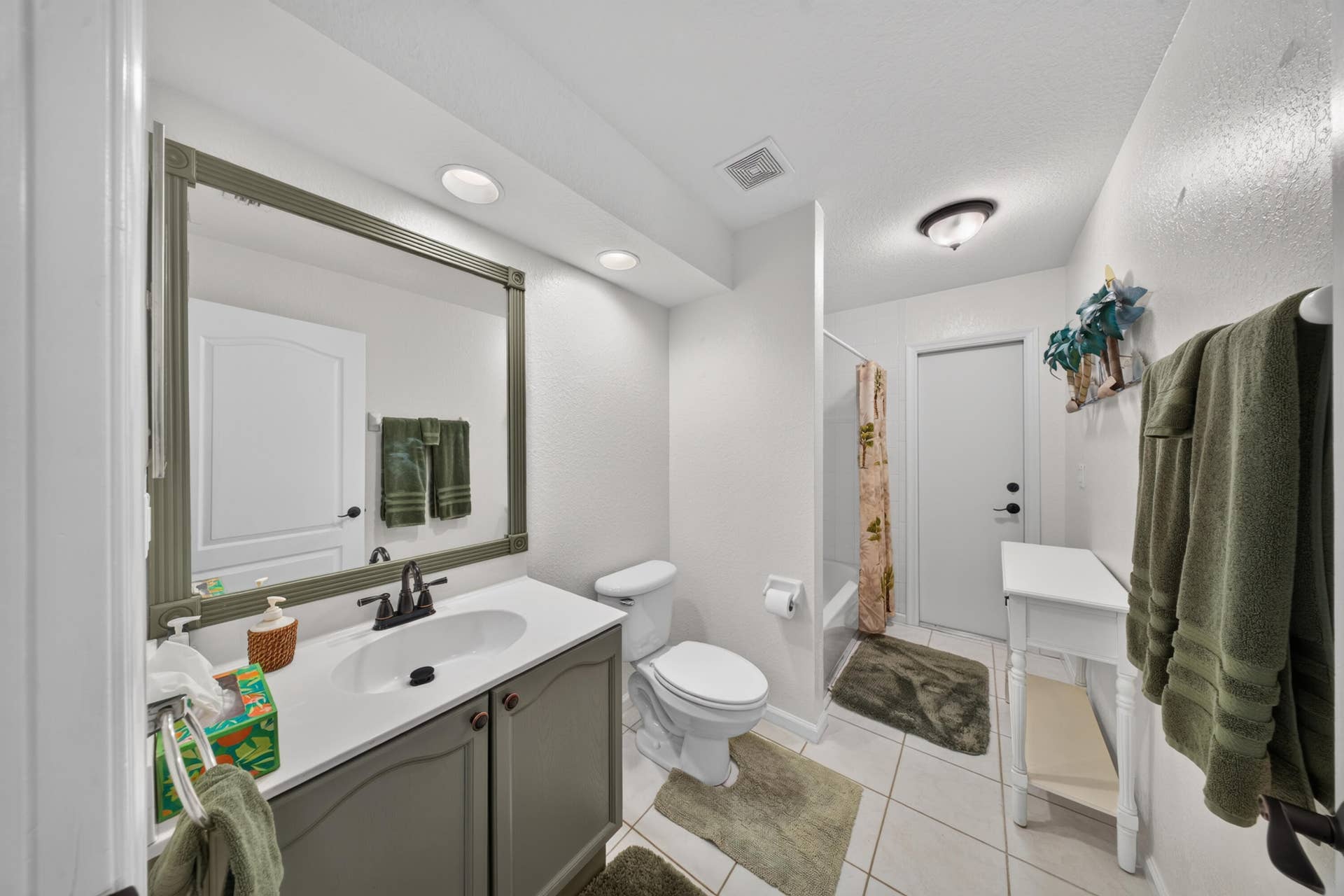 3274 SW CRUMPACKER Street, Port St Lucie, FL 34953 White tile flooring, single vanity with light countertop and gray cabinetry, framed mirror, recessed lighting, and a built-in bathtub with a shower