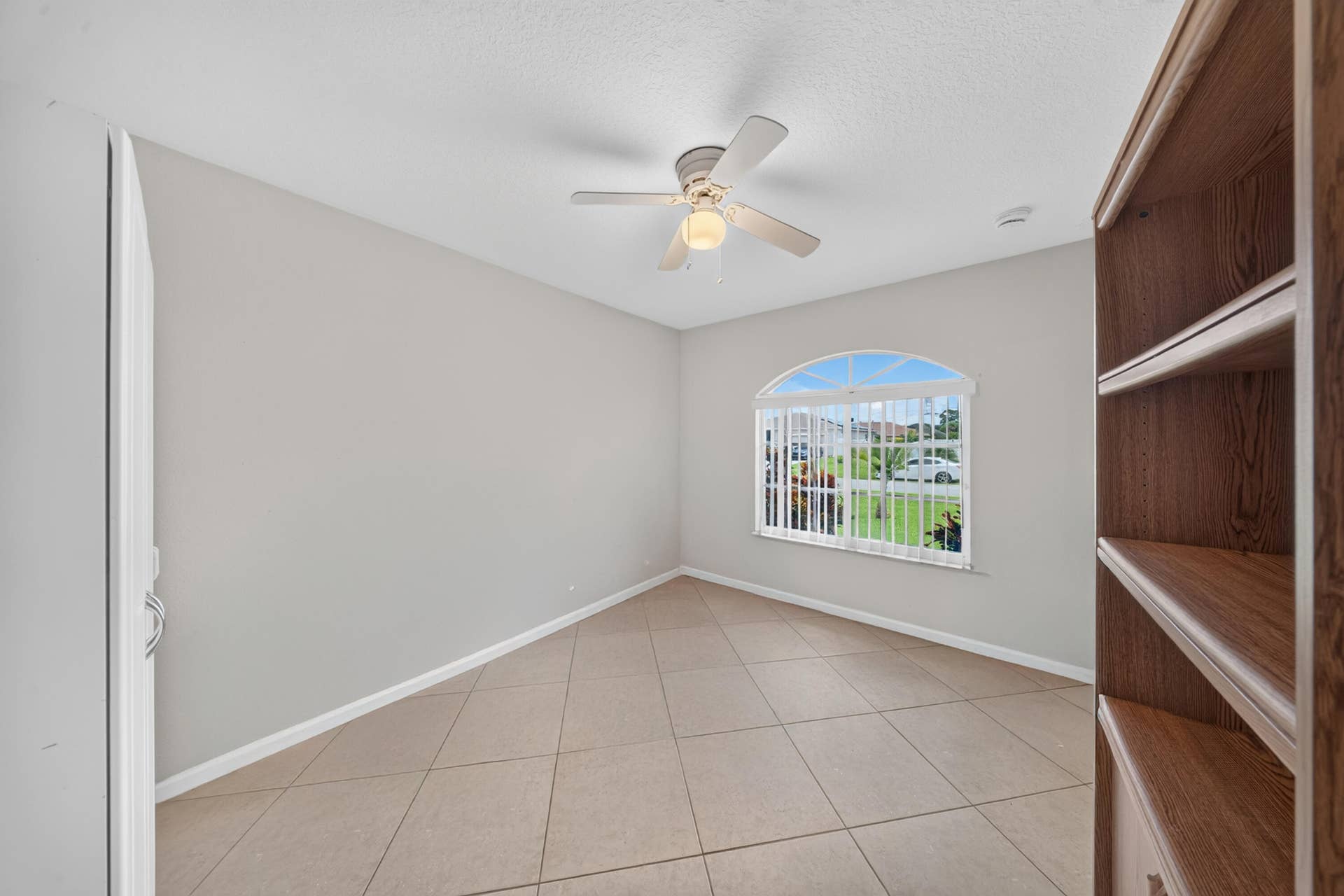 3274 SW CRUMPACKER Street, Port St Lucie, FL 34953 Arched window with blinds, ceiling fan with light fixture, light gray wall paint, and tile flooring