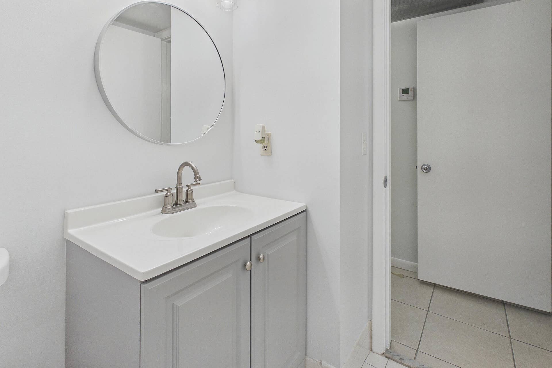 13155 SW 7TH Court, #103E, Pembroke Pines, FL 33027 White vanity with a single basin sink, brushed nickel faucet, and a circular wall-mounted mirror