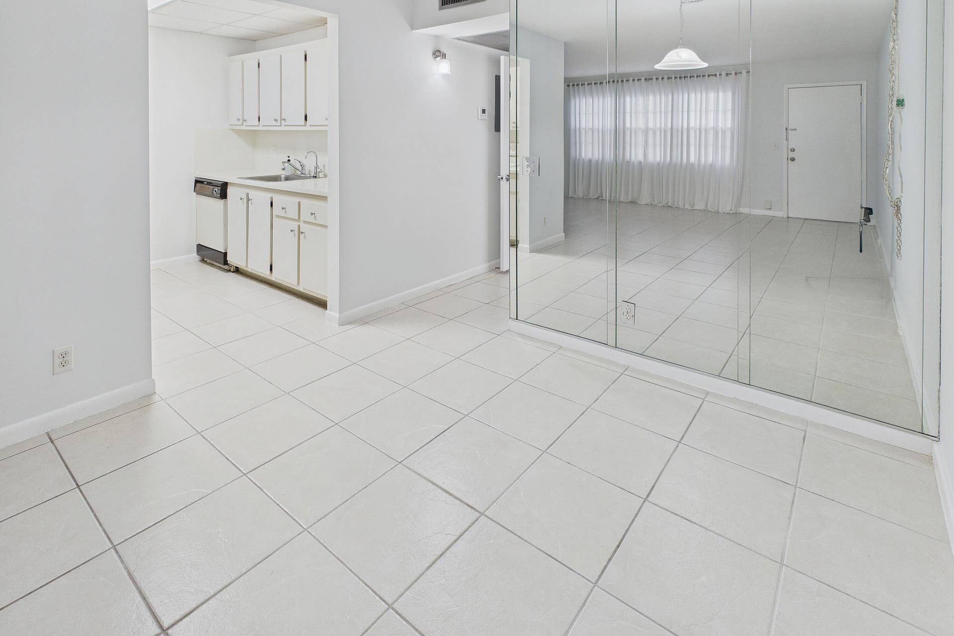 13155 SW 7TH Court, #103E, Pembroke Pines, FL 33027 Ceramic tile flooring throughout, white cabinetry, dishwasher, and full-wall mirrored accents.