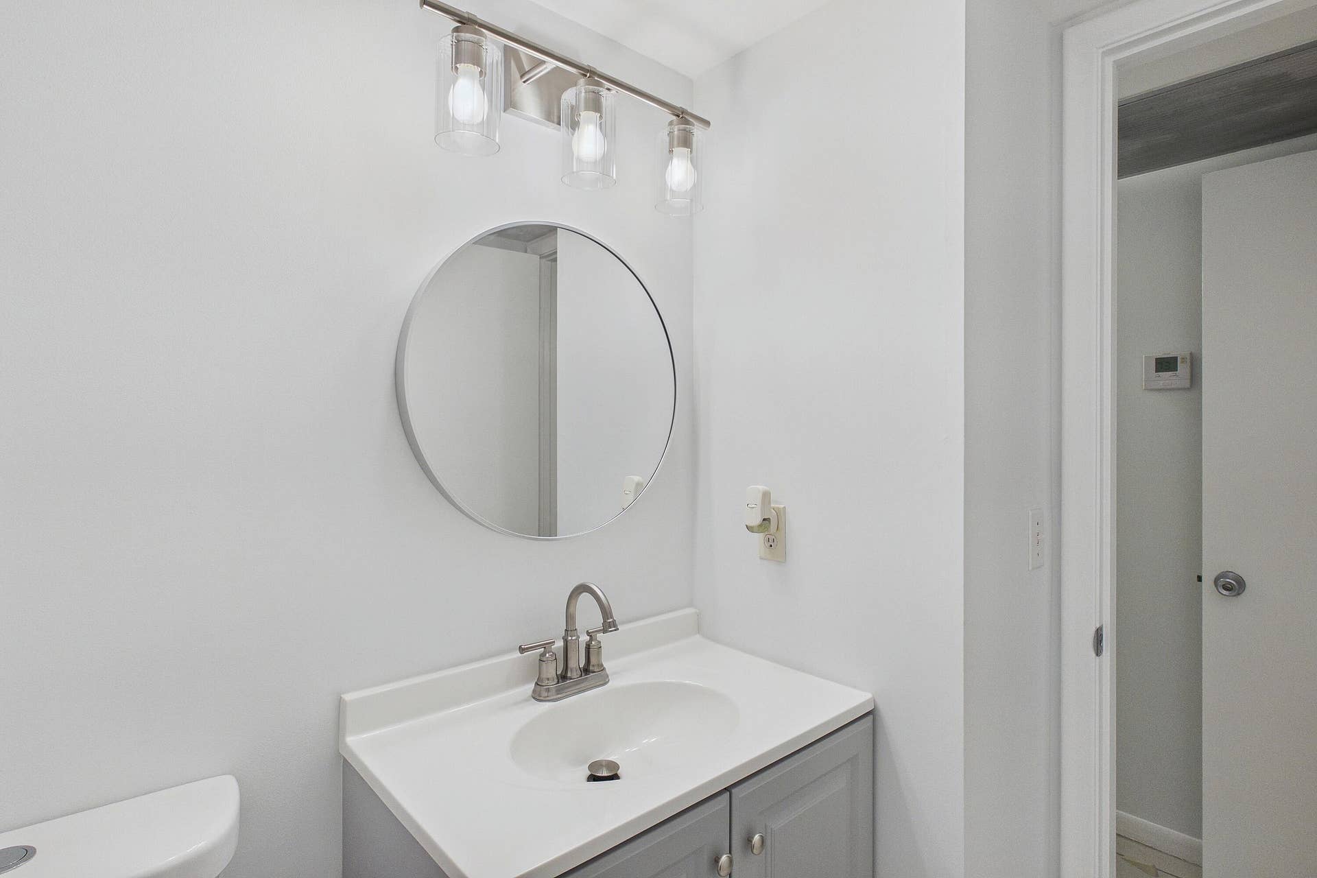 13155 SW 7TH Court, #103E, Pembroke Pines, FL 33027 Vanity with a white countertop, brushed nickel faucet, circular mirror, and three-light fixture