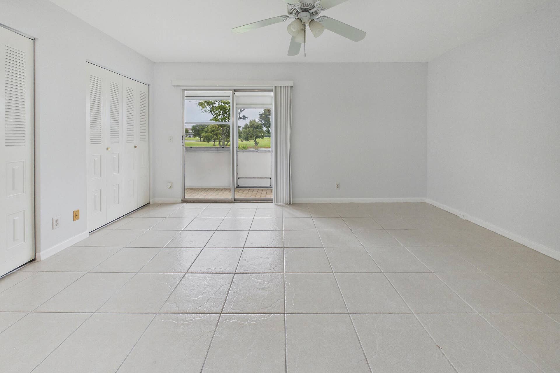 13155 SW 7TH Court, #103E, Pembroke Pines, FL 33027 Neutral tile flooring, white walls, louvered closet doors, ceiling fan, and sliding glass door with outdoor access
