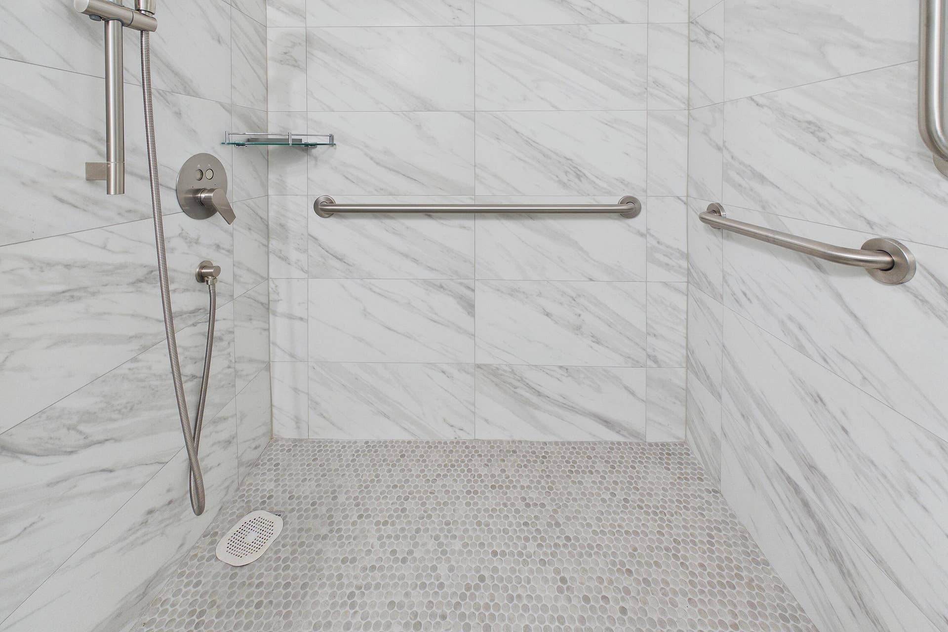13155 SW 7TH Court, #103E, Pembroke Pines, FL 33027 Renovated handicap accessible white marble-look wall tile, pebble-finish shower floor, brushed nickel shower fixtures, glass shower shelf, and integrated grab bars