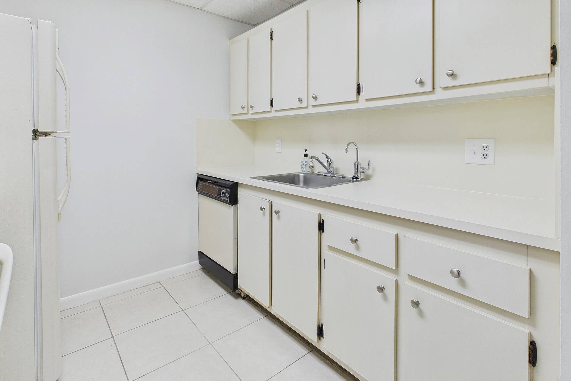 13155 SW 7TH Court, #103E, Pembroke Pines, FL 33027 White cabinetry with chrome hardware, an integrated stainless steel sink, a dishwasher, and a refrigerator