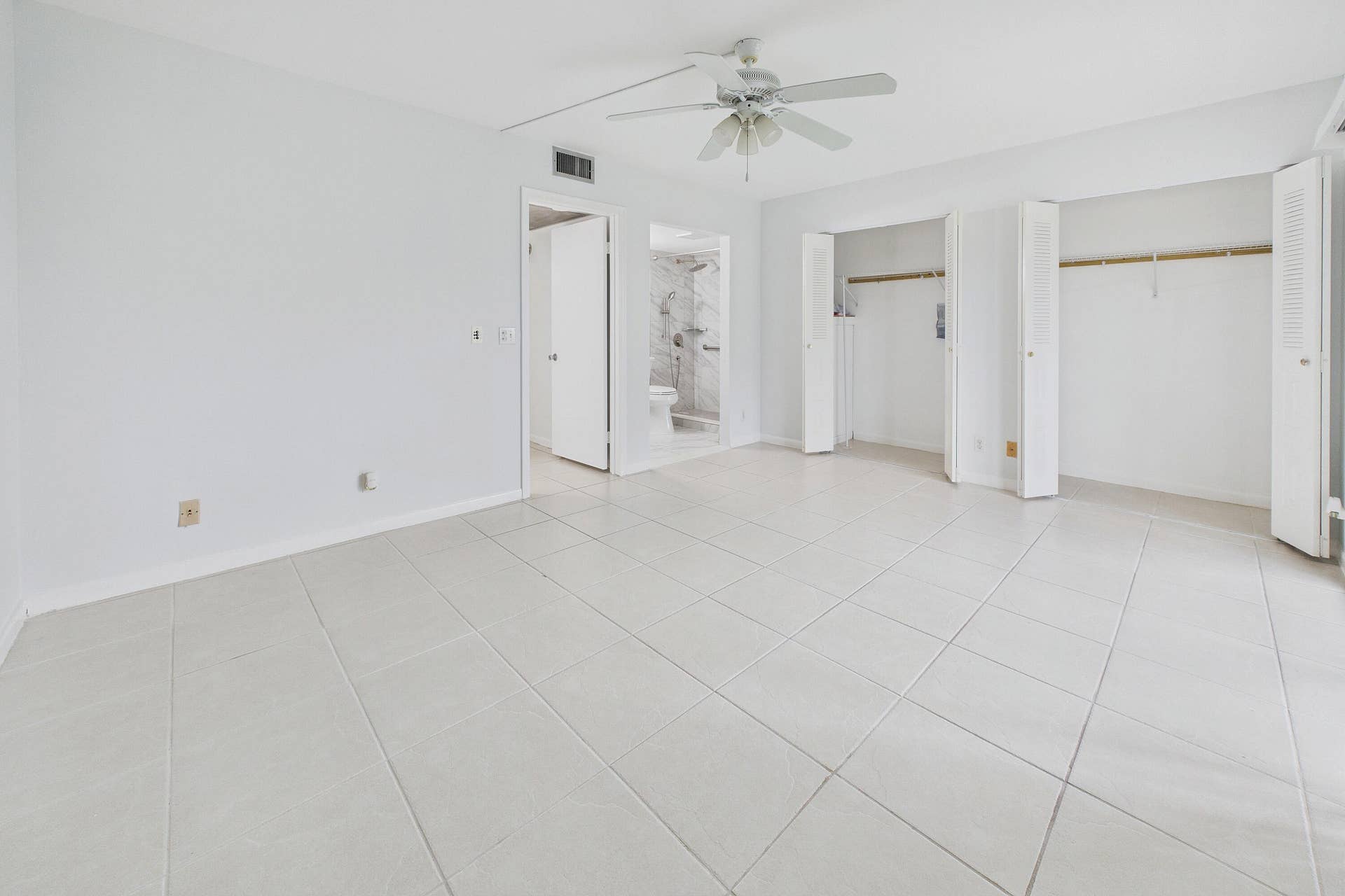 13155 SW 7TH Court, #103E, Pembroke Pines, FL 33027 White tile flooring, dual bi-fold closet doors, ceiling fan with light fixture, and a white interior door leading to a bathroom with a tiled shower