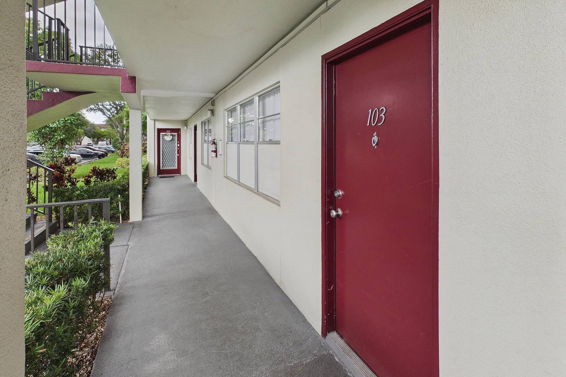 13155 SW 7TH Court, #103E, Pembroke Pines, FL 33027 Covered exterior walkway featuring a solid entry door with contrasting trim, multiple windows, and exterior foliage