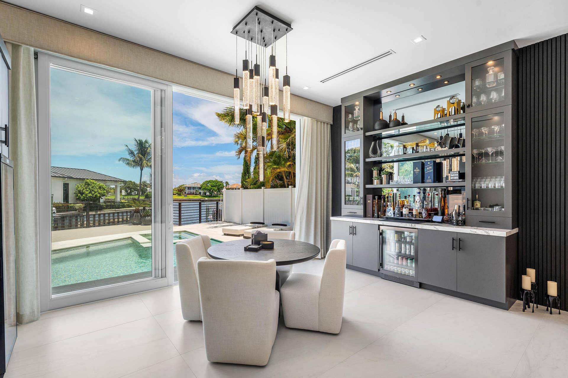 12898 S Shore Drive, Palm Beach Gardens, FL 33410 Floor-to-ceiling sliding glass doors, built-in wet bar with mirrored backsplash, integrated beverage refrigerator, modern pendant lighting, and light-toned tile flooring