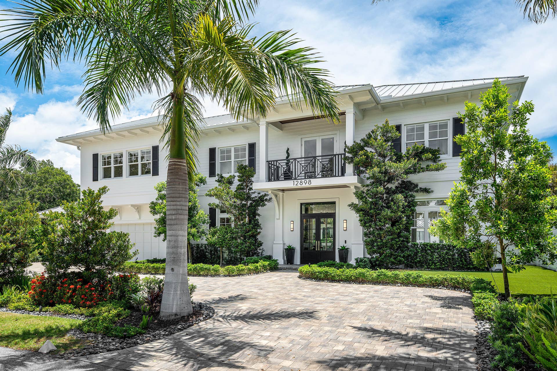 12898 S Shore Drive, Palm Beach Gardens, FL 33410 Two-story white exterior with dark shutters, metal roof, and an oversized paved circular driveway