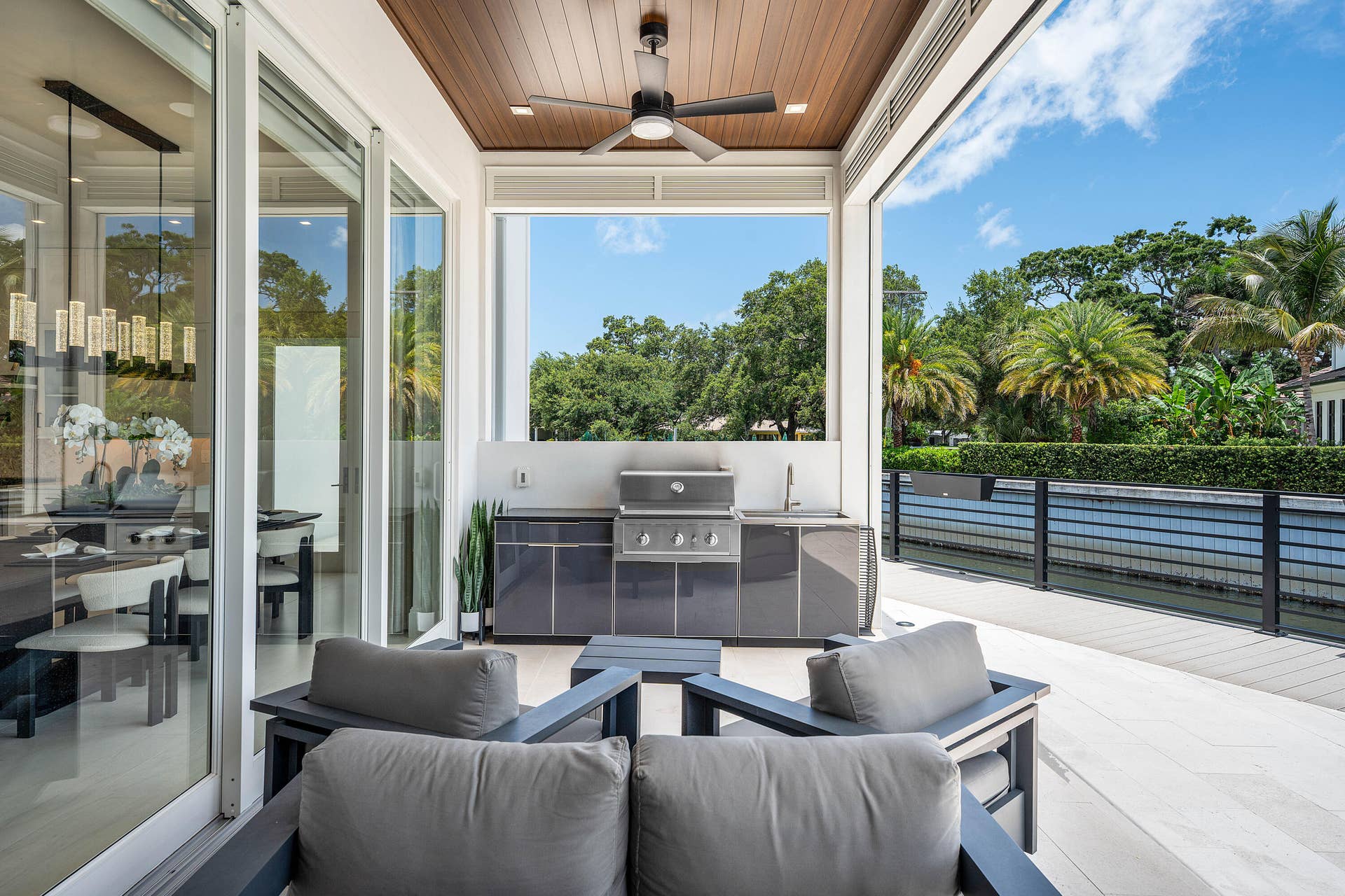 12898 S Shore Drive, Palm Beach Gardens, FL 33410 Expansive outdoor living area with wood-finish ceiling, built-in outdoor kitchen with grill and sink, ceiling fan, and large sliding glass doors