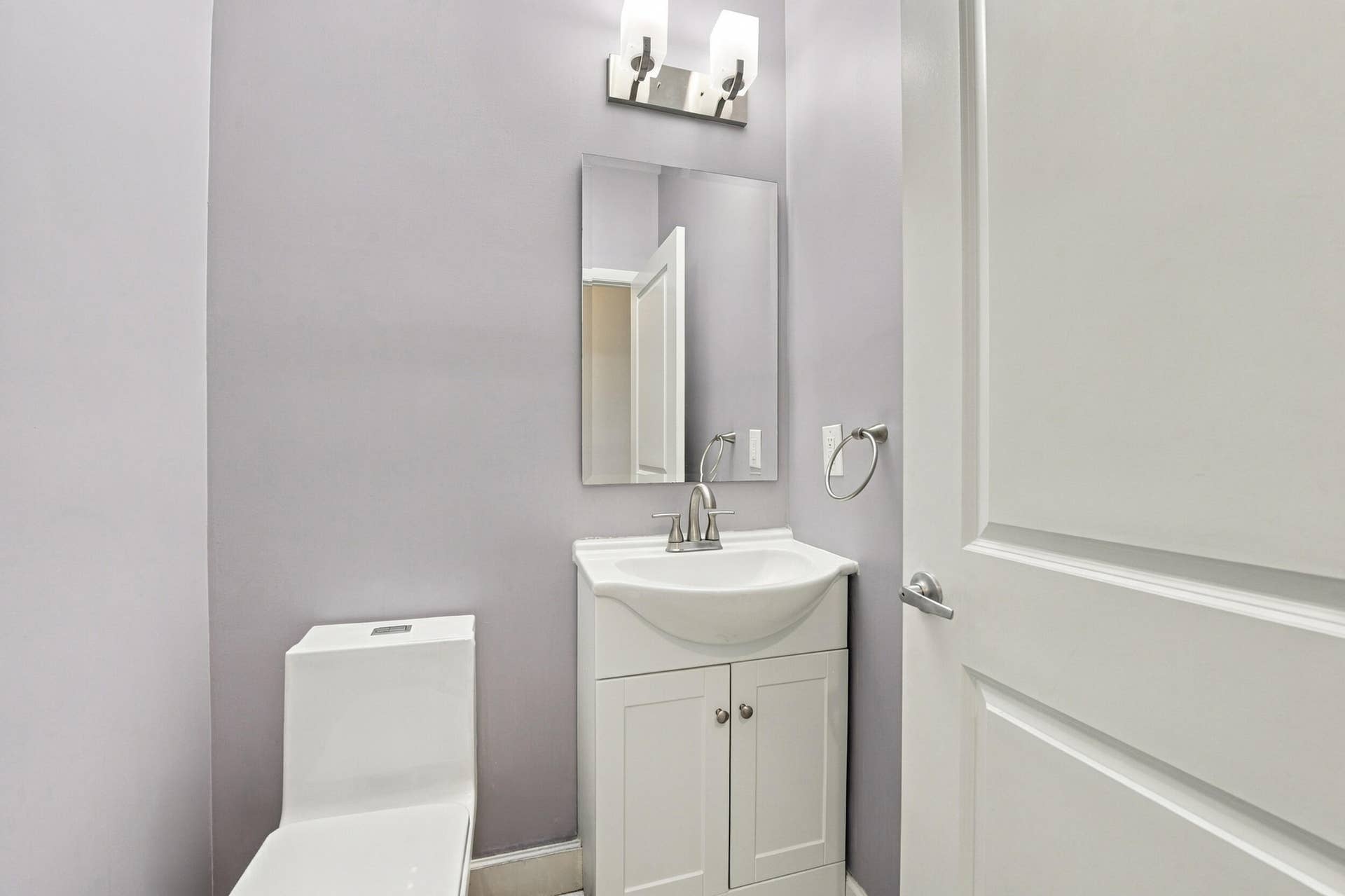 Vanity with integrated sink, white cabinetry, wall-mounted mirror, modern lighting fixture, and panel door