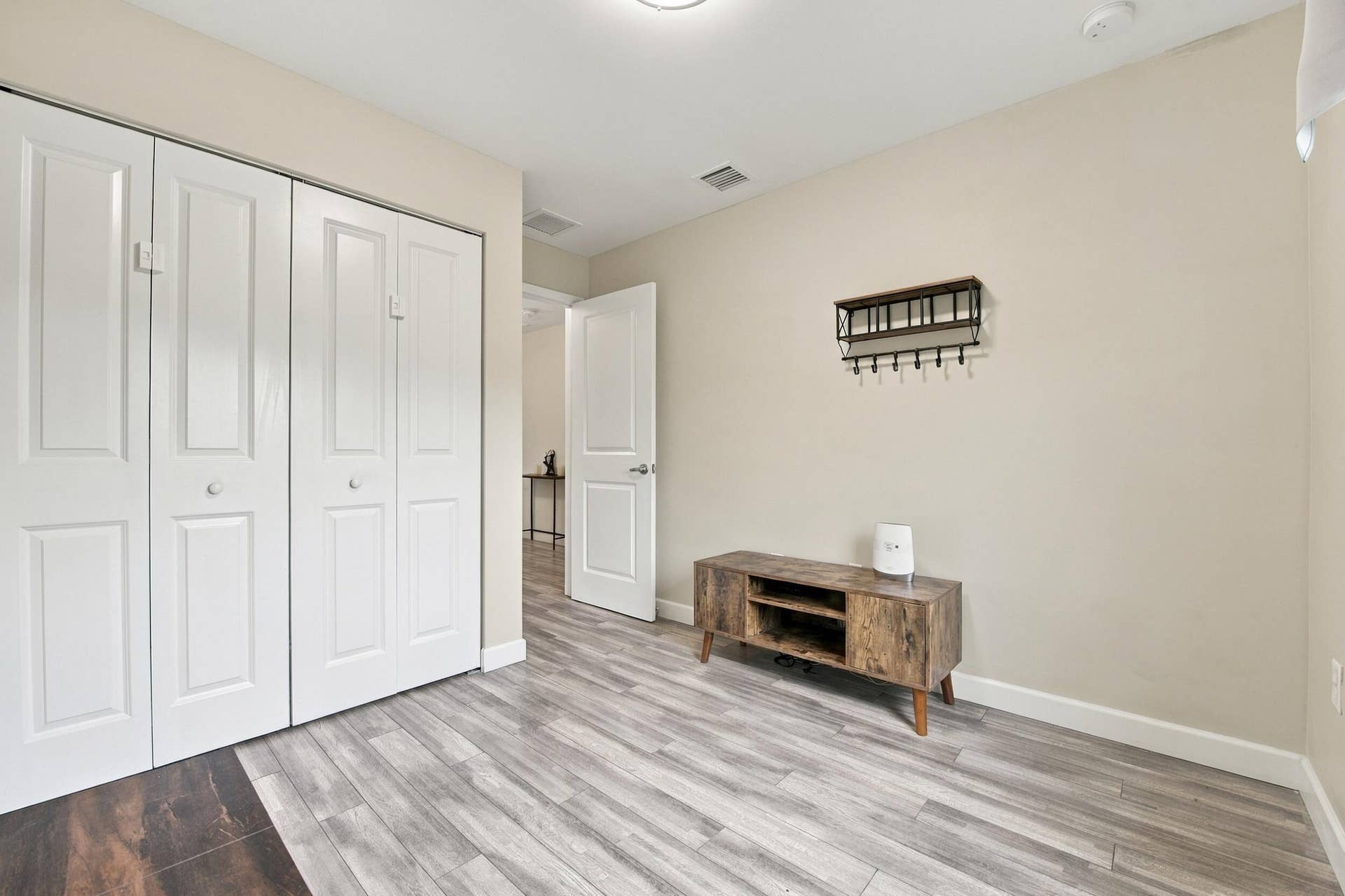 Neutral wall color, wood-finish flooring, white bi-fold closet doors, white baseboards, and a white interior door with a silver-tone knob