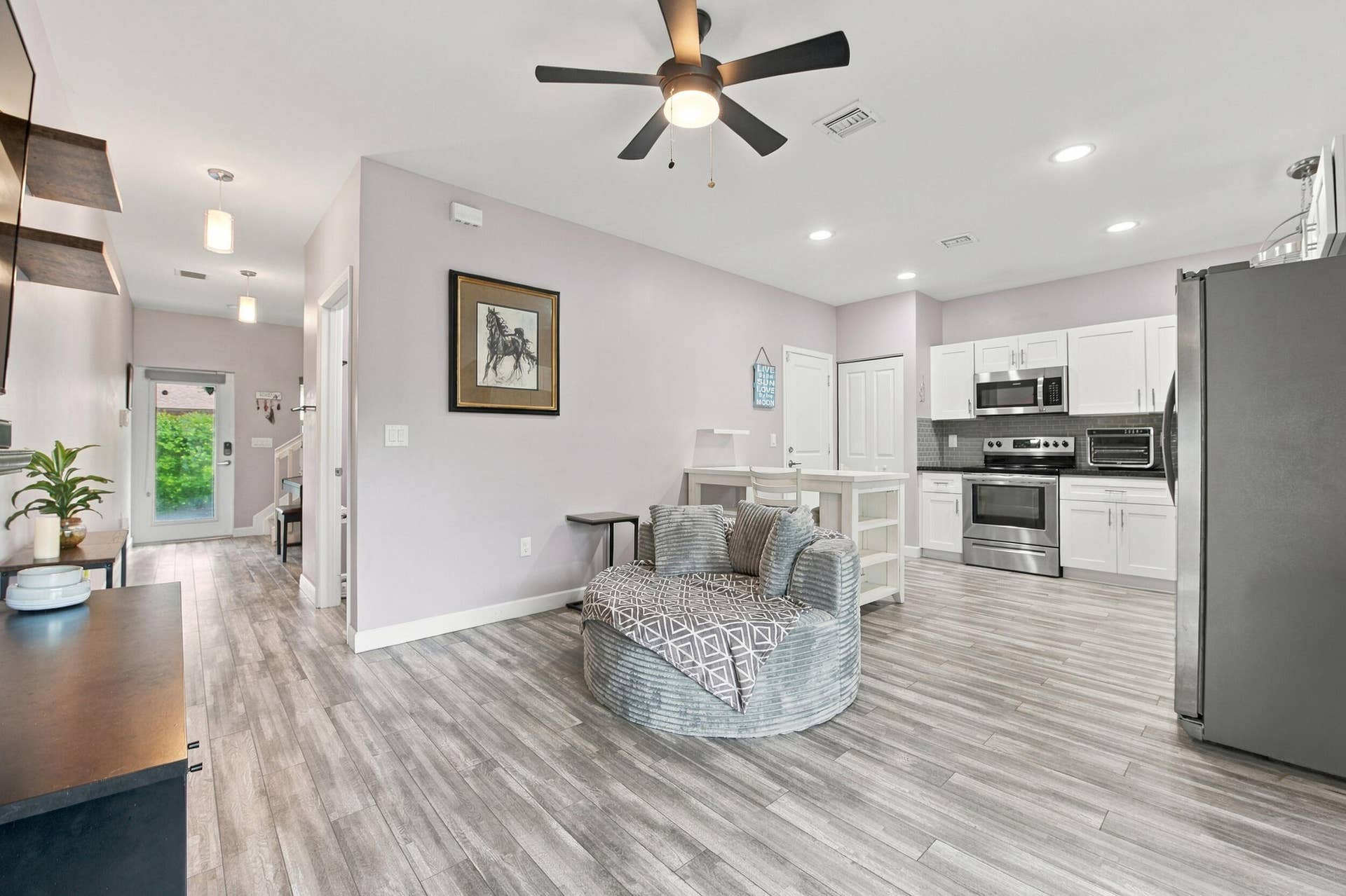 Open-concept living area with wood-finish flooring, white cabinetry, stainless steel appliances, and recessed lighting