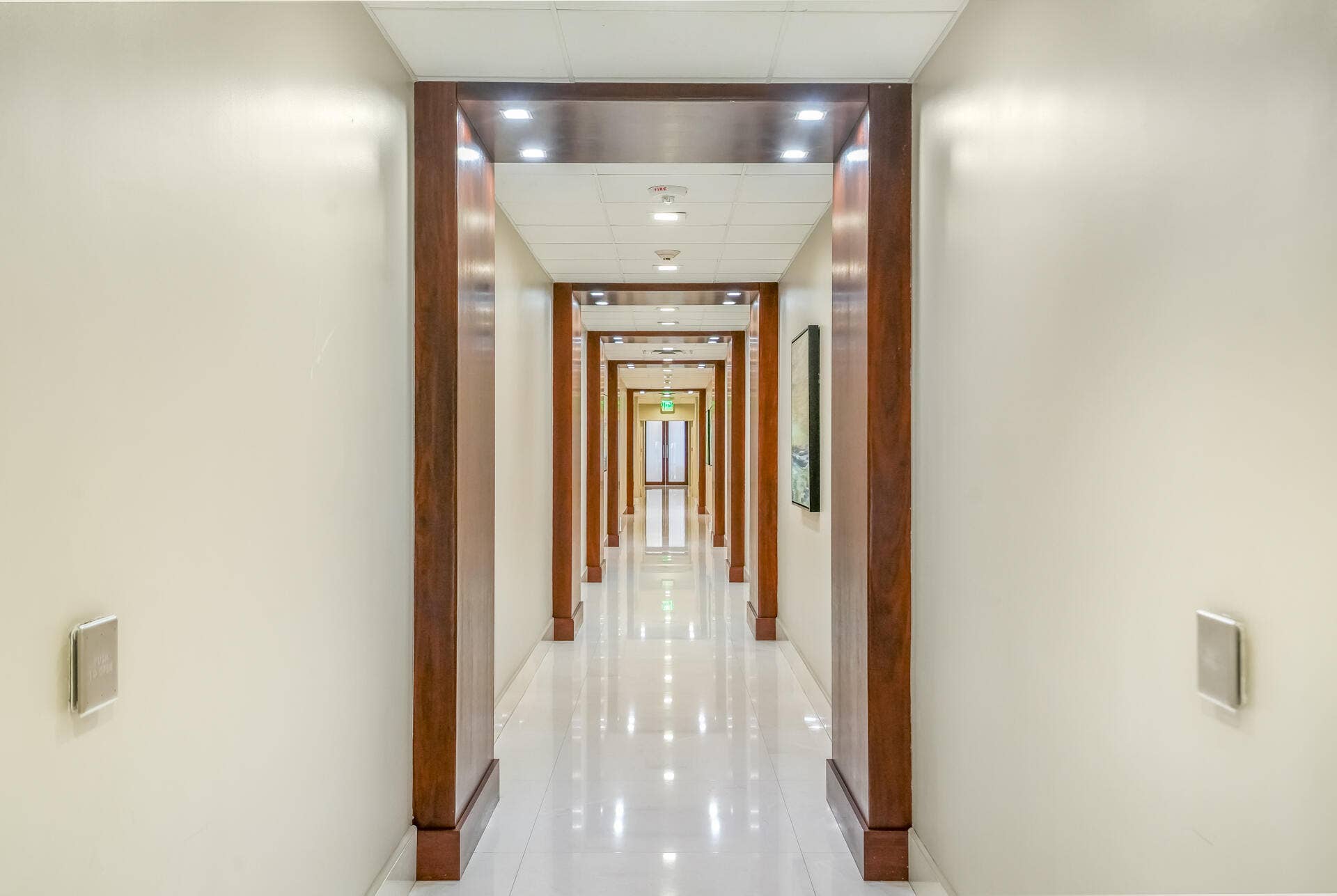 Long hallway featuring wood-finish door frames, recessed ceiling lighting, and polished flooring