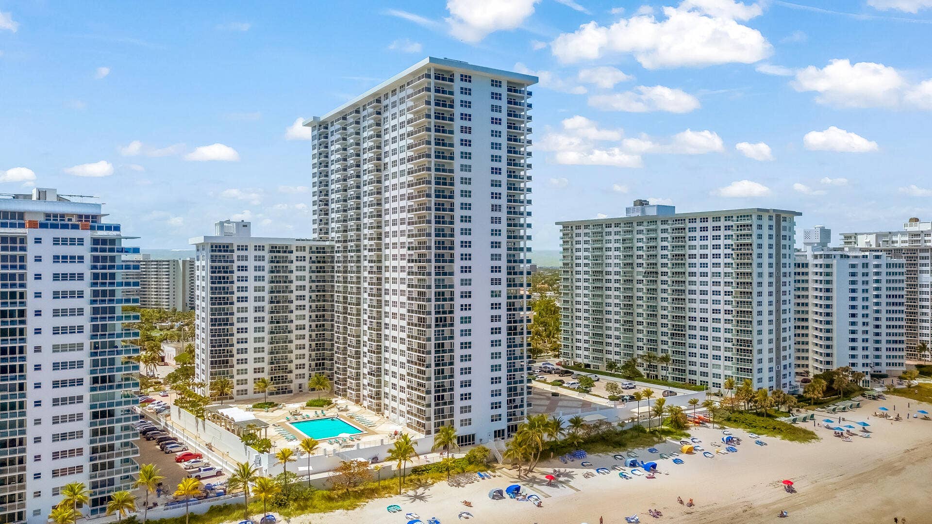 High-rise building with multiple balconies, a ground-level swimming pool, and direct beach access