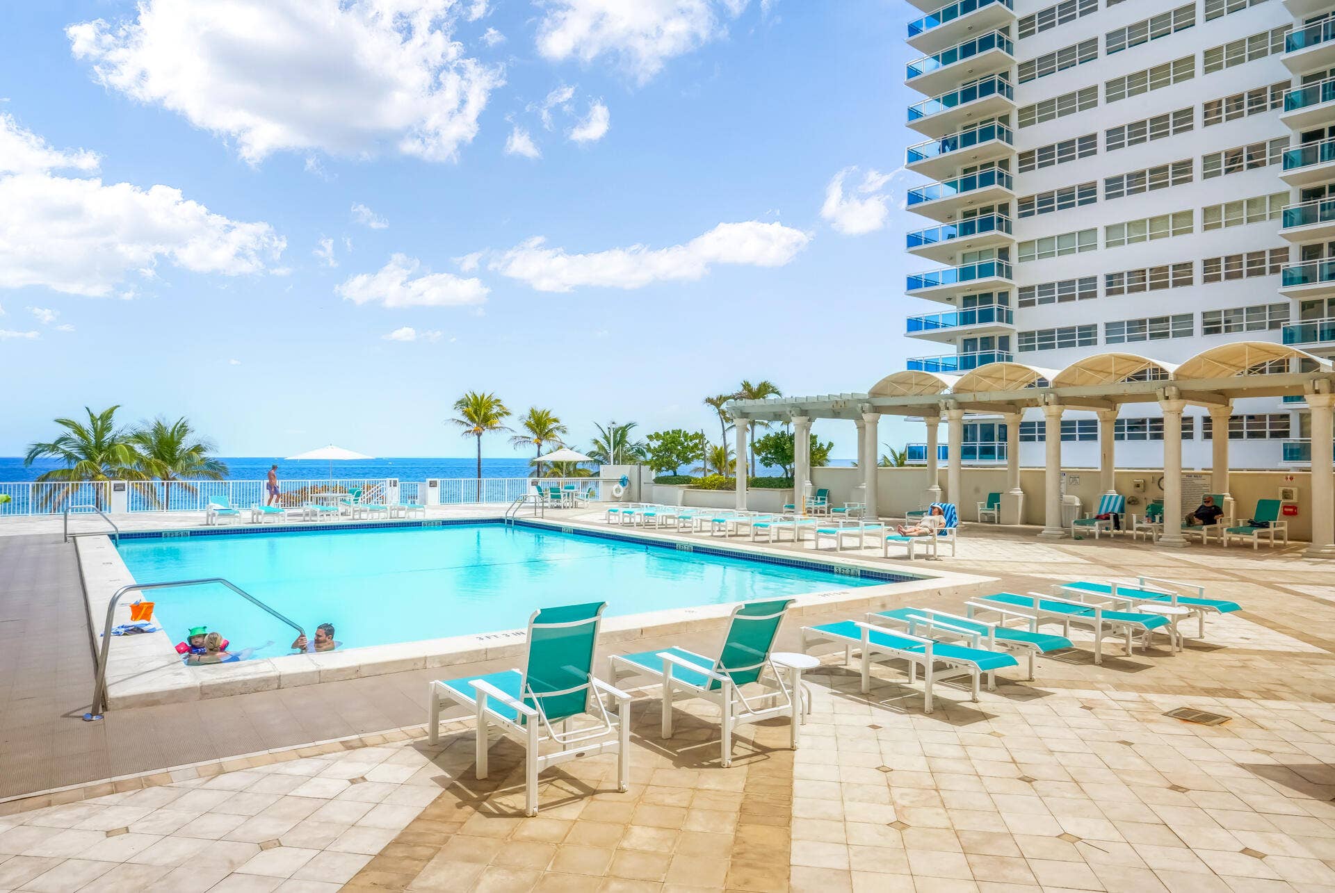 3500 Galt Ocean Drive, #807, Fort Lauderdale, FL 33308 Resort-style oceanfront pool deck with expansive sun lounging area, featuring turquoise waters, palm landscaping, covered cabana structures with yellow archways, and direct beachfront access with unobstructed ocean vistas