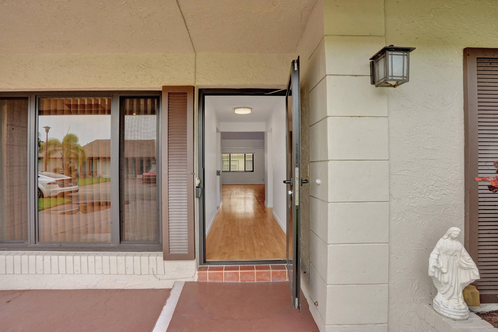 Covered entry with exterior wall sconce, full-light entry door, sidelight window, and wood-finish flooring