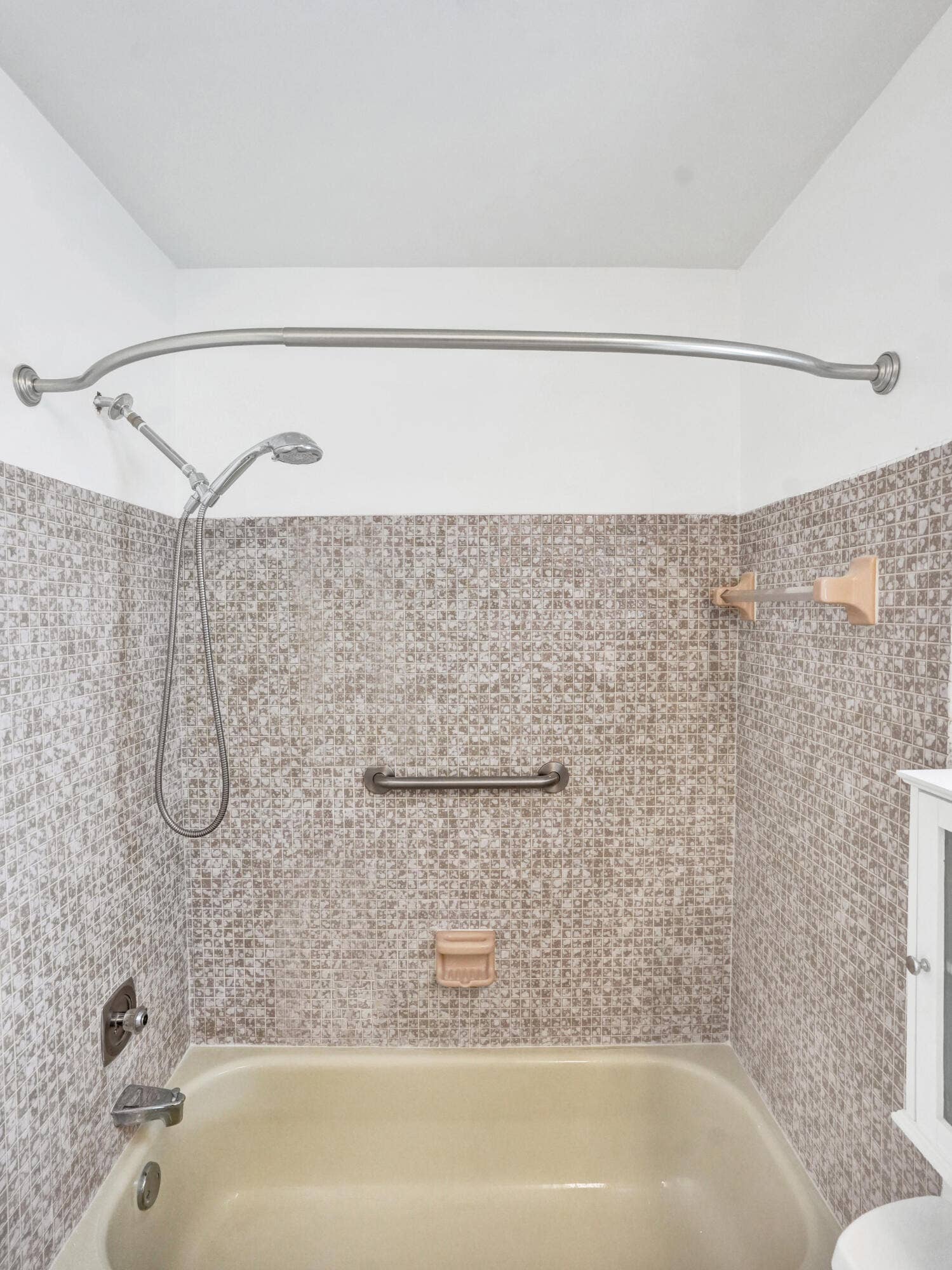 Bathtub with mosaic tile surround, curved shower rod, and integrated grab bar