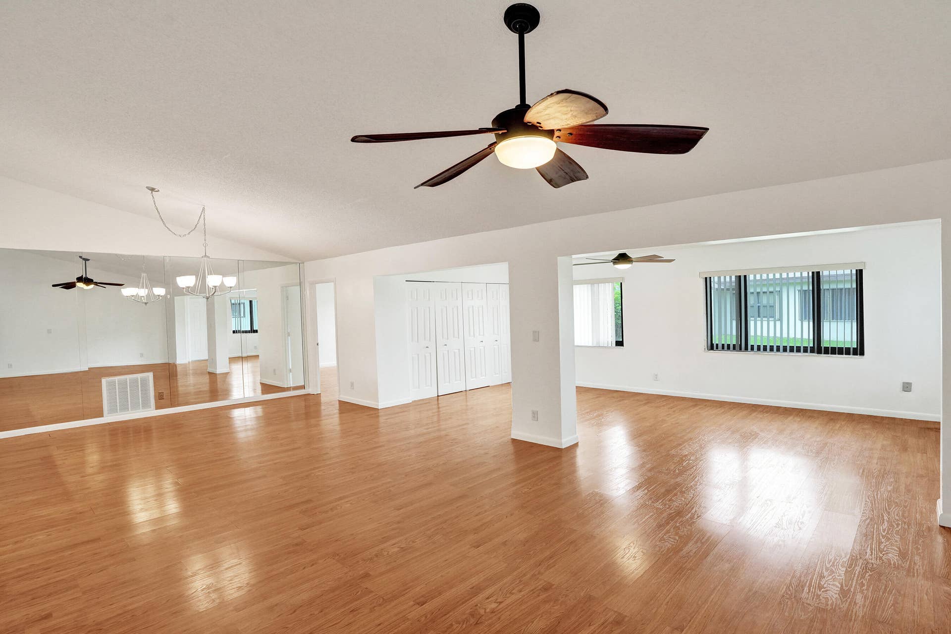 Vaulted ceiling with a ceiling fan, wood-finish flooring, mirrored wall, built-in storage, and multiple windows