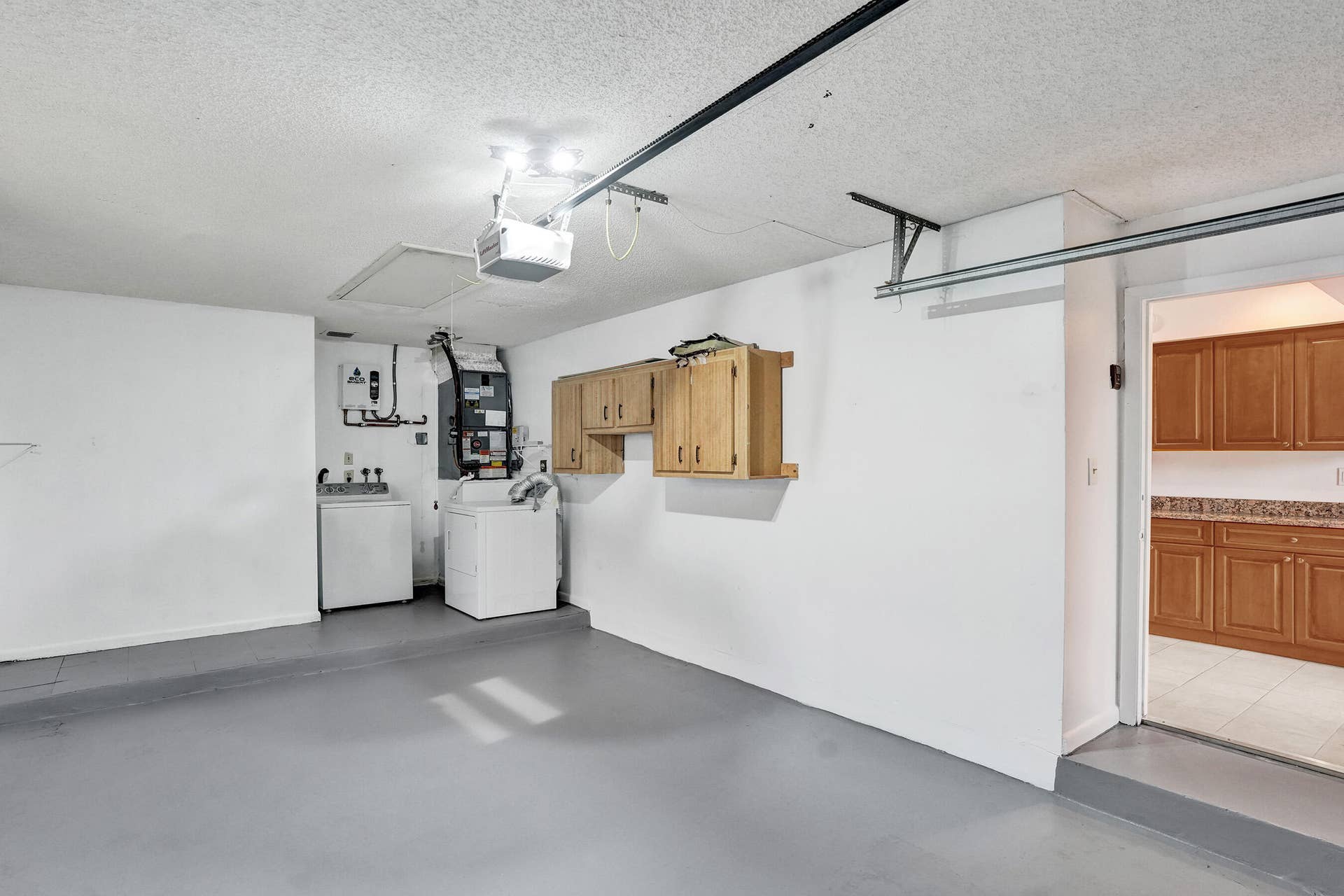 Spacious garage with light wood-finish cabinetry, a utility sink, and laundry appliances