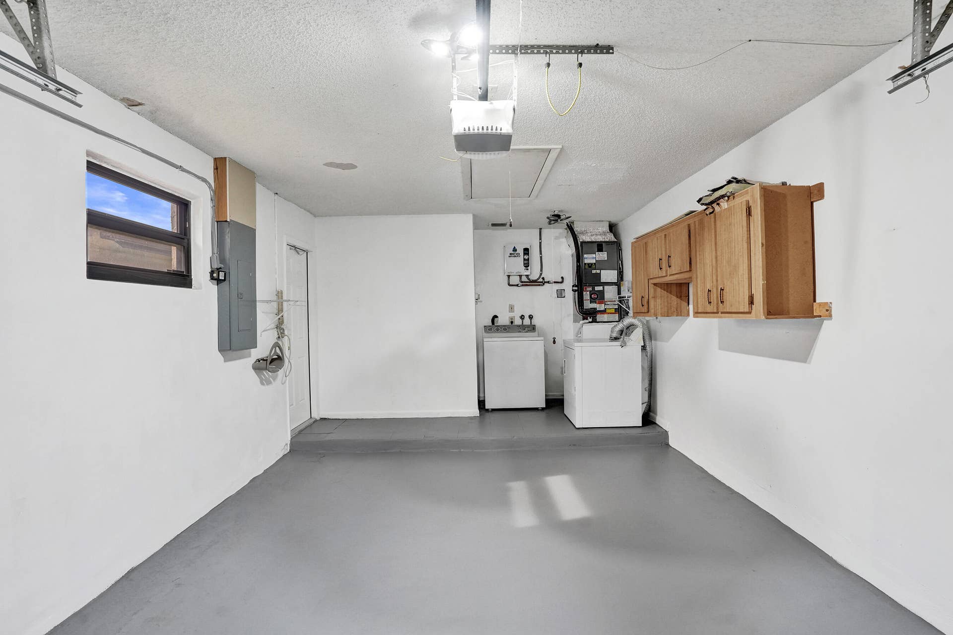 Utility area with painted concrete flooring, wall-mounted cabinetry, and a window for natural light