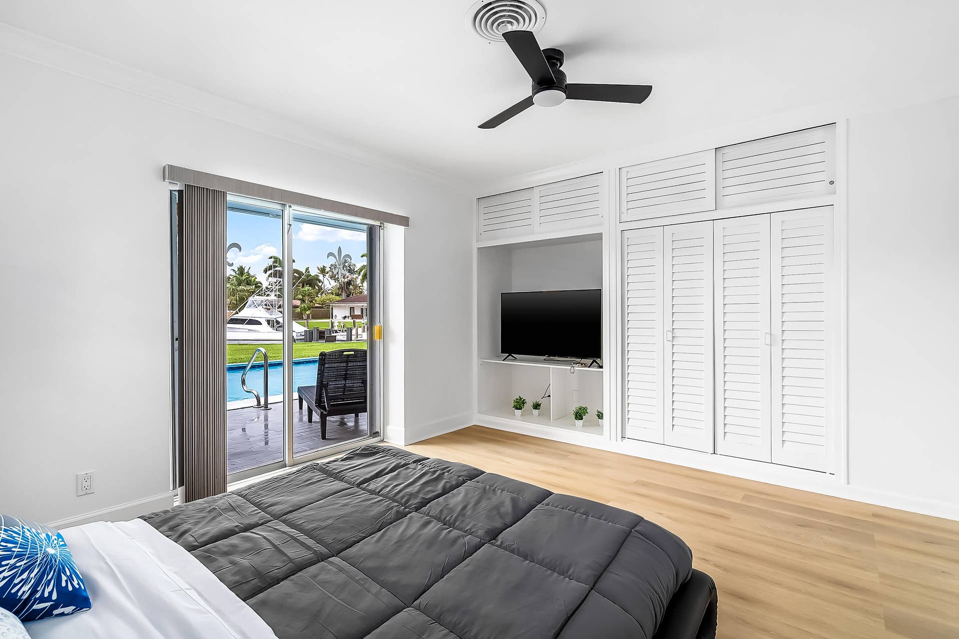1250 SE 10TH Street, Deerfield Beach, Deerfield Beach, FL 33441 Sliding glass doors opening to a pool and waterway, featuring light wood-finish flooring, a contemporary ceiling fan, and built-in cabinetry with louvered doors