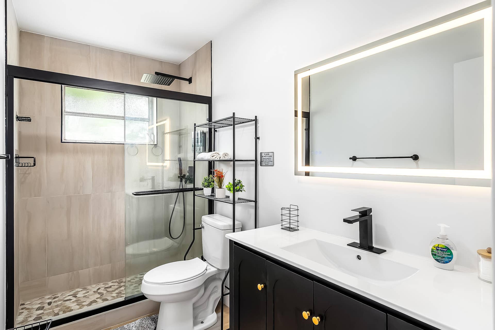 1250 SE 10TH Street, Deerfield Beach, Deerfield Beach, FL 33441 Contemporary bathroom featuring an illuminated vanity mirror, a black single-handle faucet, and a black vanity with gold-tone hardware