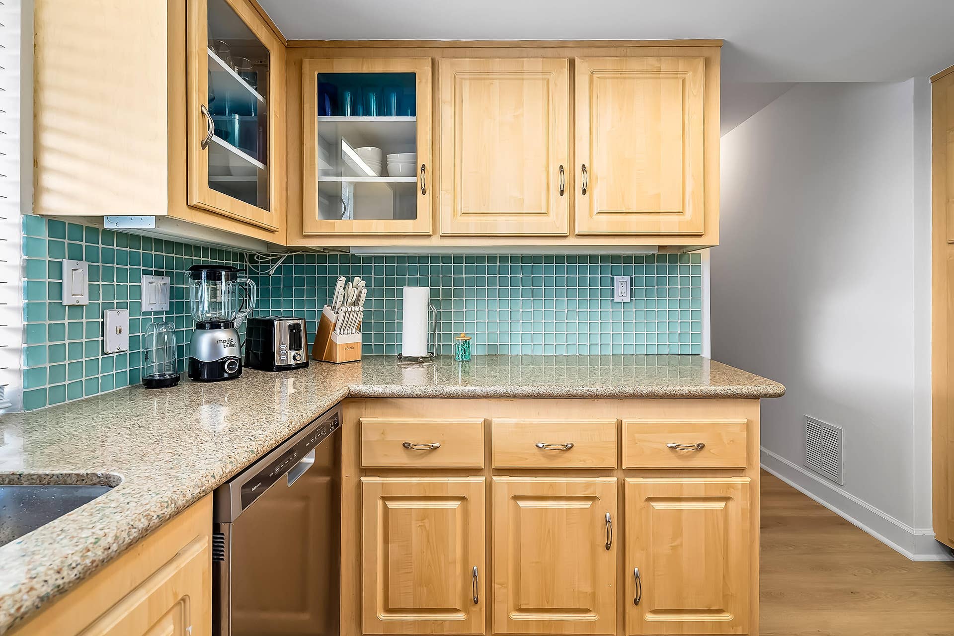 1250 SE 10TH Street, Deerfield Beach, Deerfield Beach, FL 33441 Kitchen featuring light wood cabinetry with glass-front accents, granite-style countertops, a blue-green tile backsplash, and stainless steel dishwasher