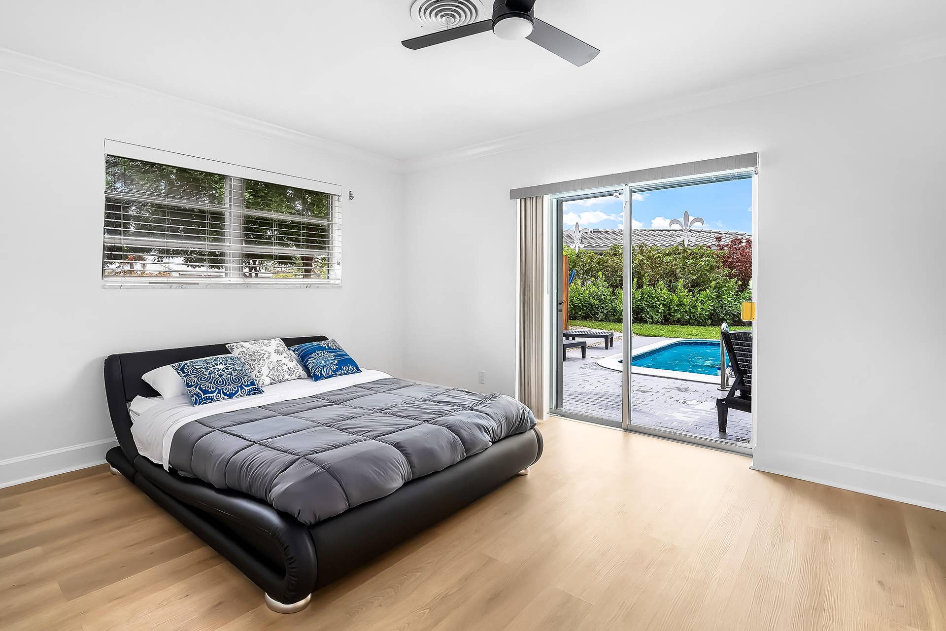 1250 SE 10TH Street, Deerfield Beach, Deerfield Beach, FL 33441 Wood-finish flooring throughout, featuring a ceiling fan, window with horizontal blinds, and a sliding glass door opening to a paved patio and in-ground pool