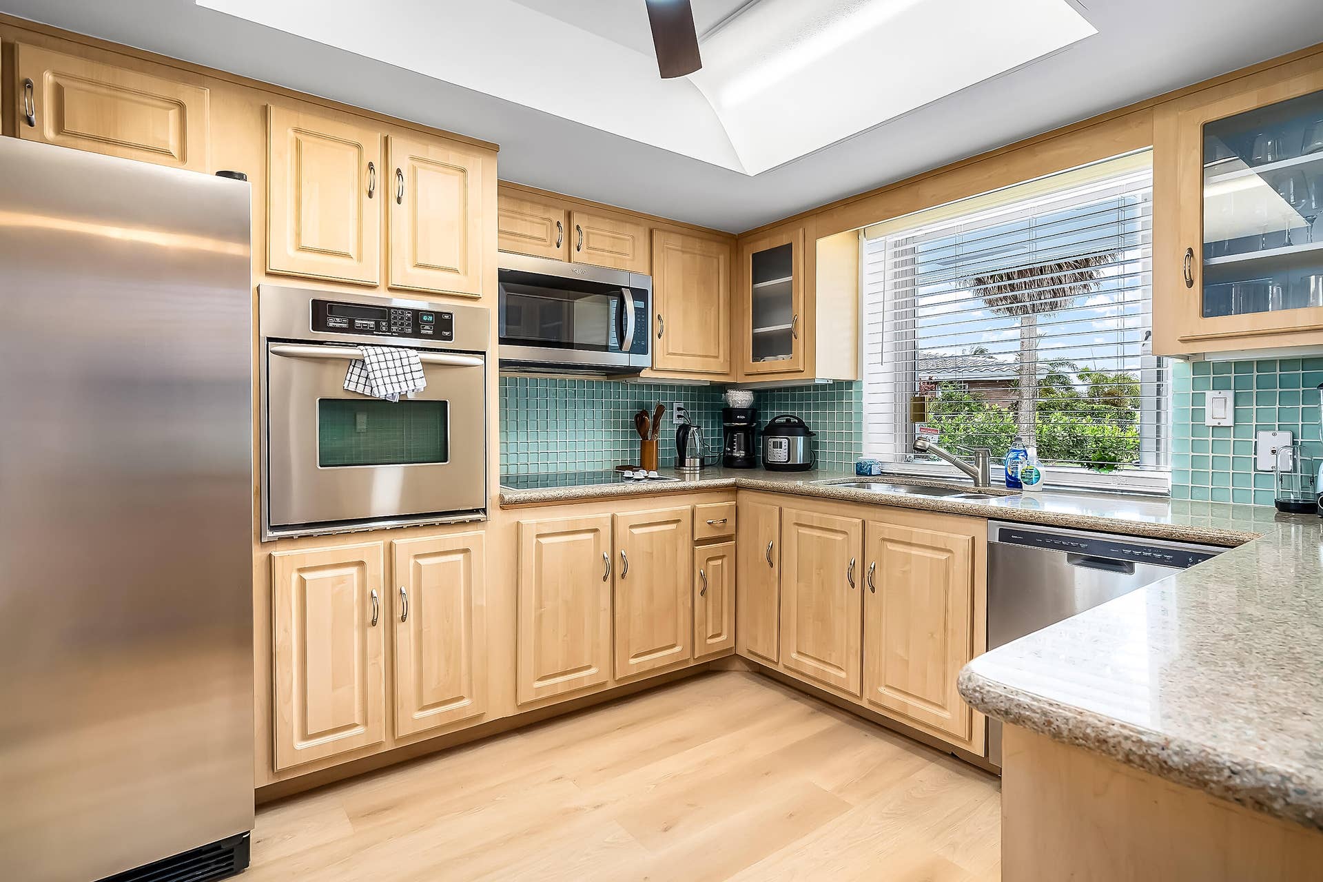 1250 SE 10TH Street, Deerfield Beach, Deerfield Beach, FL 33441 Kitchen featuring light wood-finish cabinetry, stainless steel appliances including a built-in oven and microwave, stone-finish countertops, and a tiled backsplash