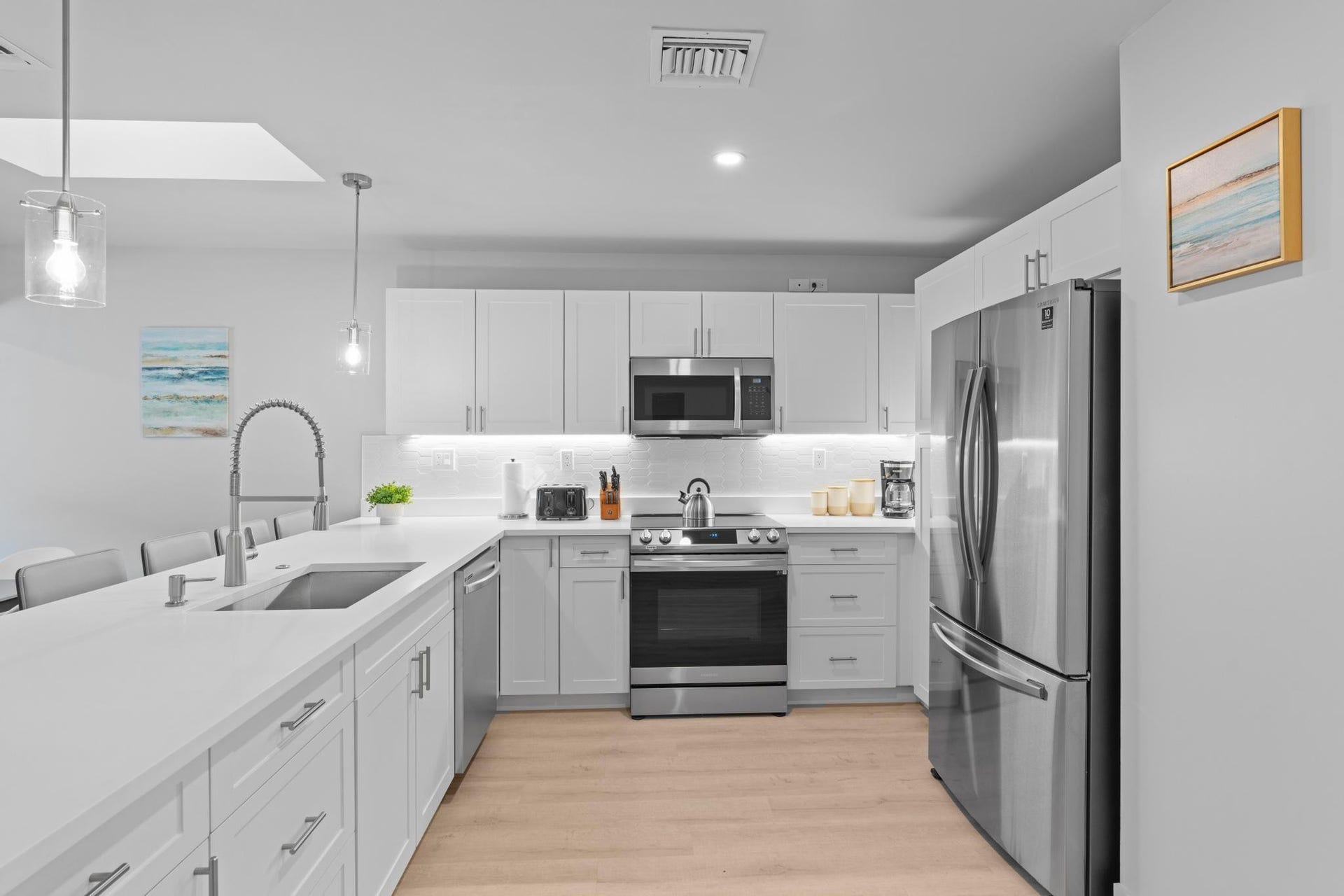 Modern kitchen featuring white cabinetry, stainless steel appliances, a large island with an undermount sink, and wood-finish flooring
