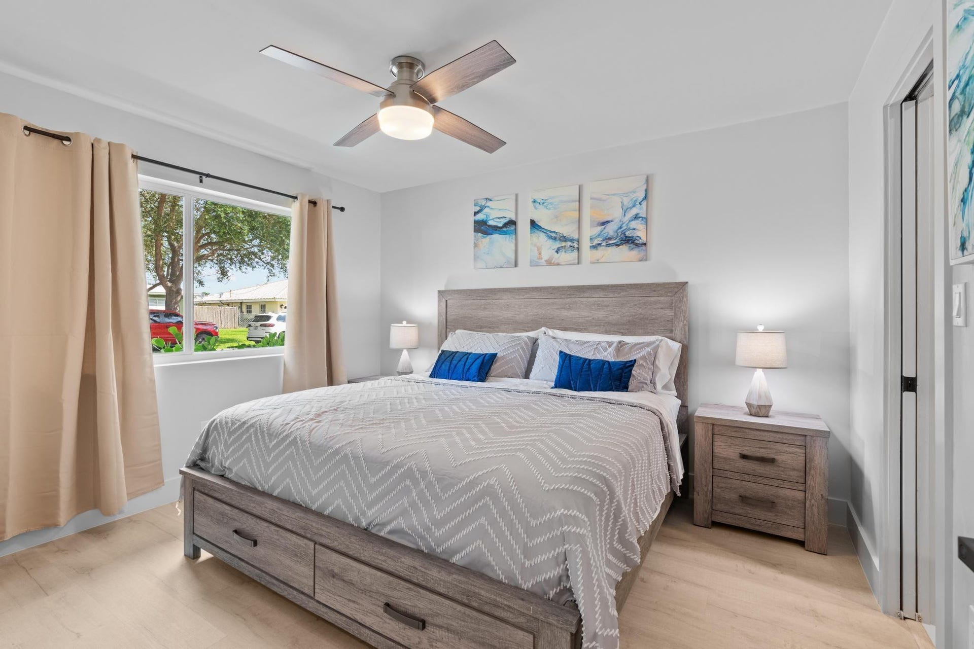 Light wood-finish flooring, a ceiling fan with integrated lighting, and a window with white trim