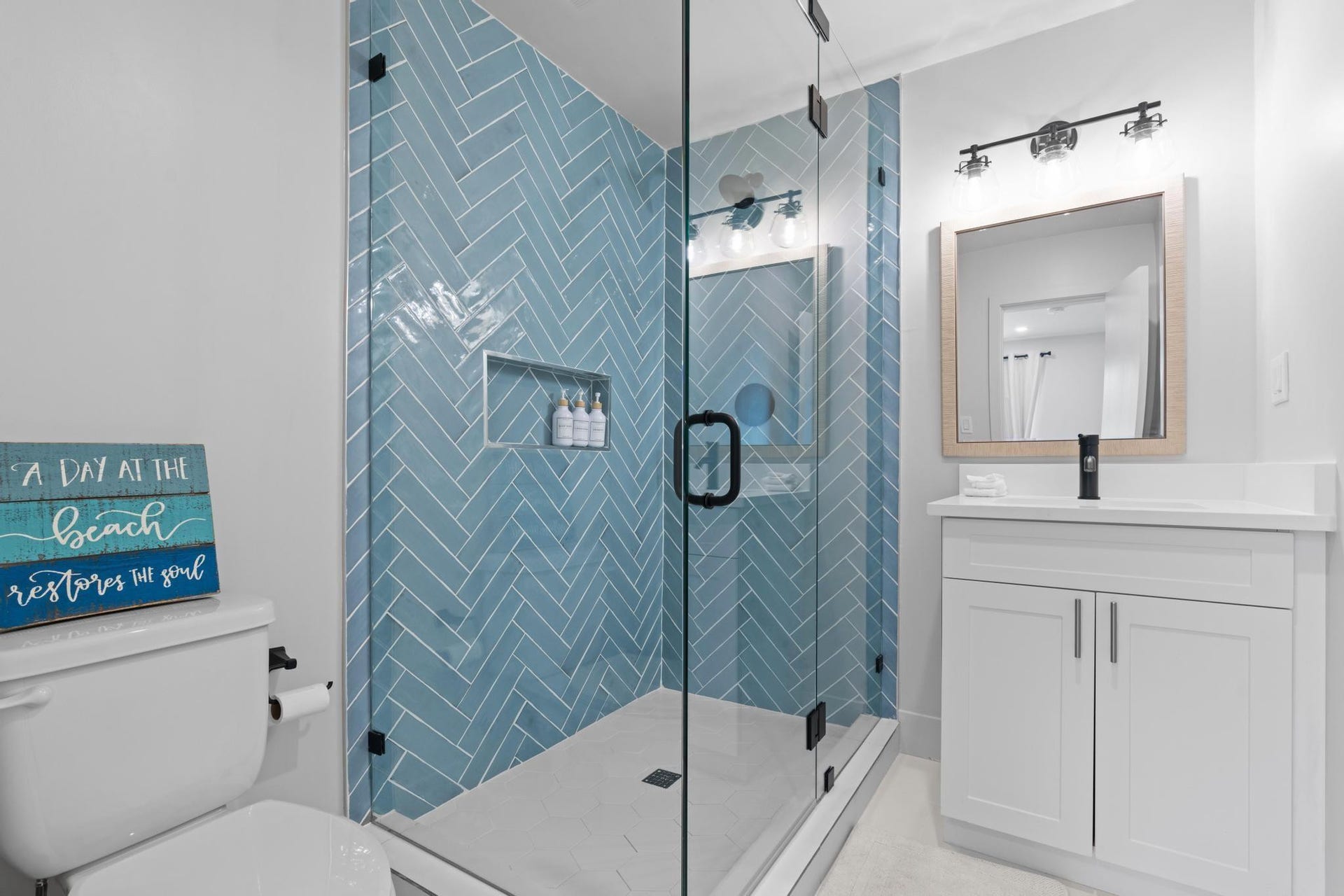 Glass-enclosed shower with herringbone tile, white vanity with integrated sink, and modern black hardware