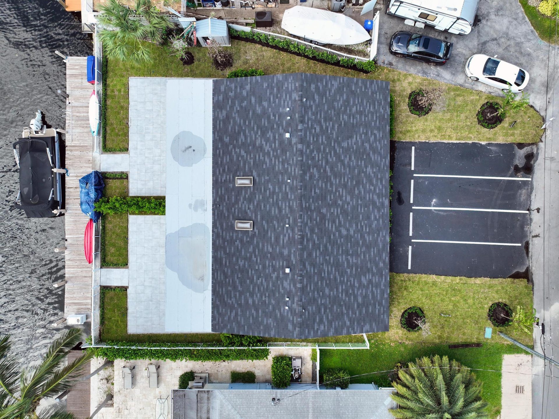 Waterfront property featuring a dark shingle roof, expansive dock, and multi-space paved parking