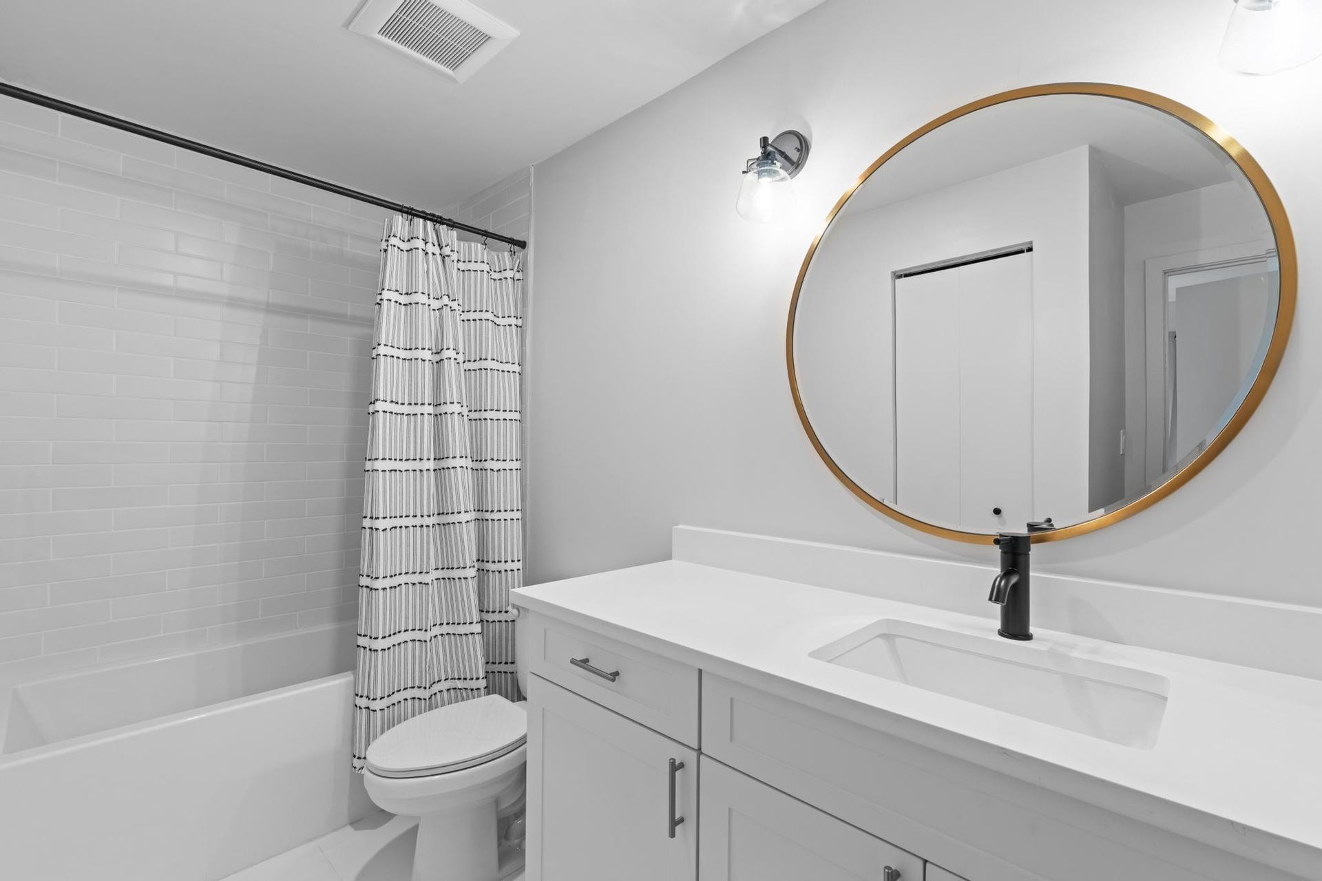 Bathroom featuring a white subway tile tub surround, white vanity with an integrated sink, matte black faucet, and a round gold-framed mirror