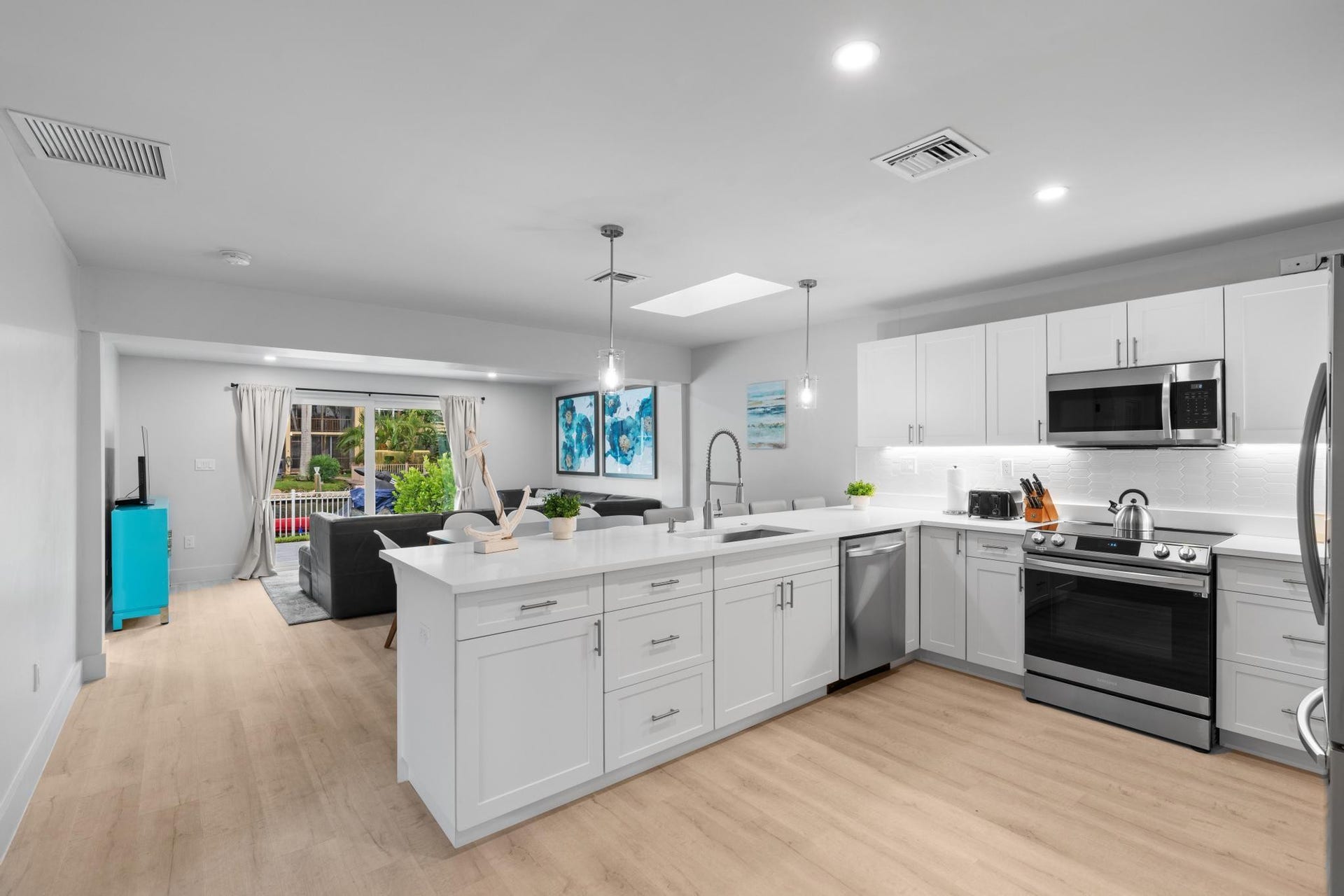 Kitchen featuring a large island with pendant lighting, white cabinetry, integrated stainless steel appliances, and wood-finish flooring