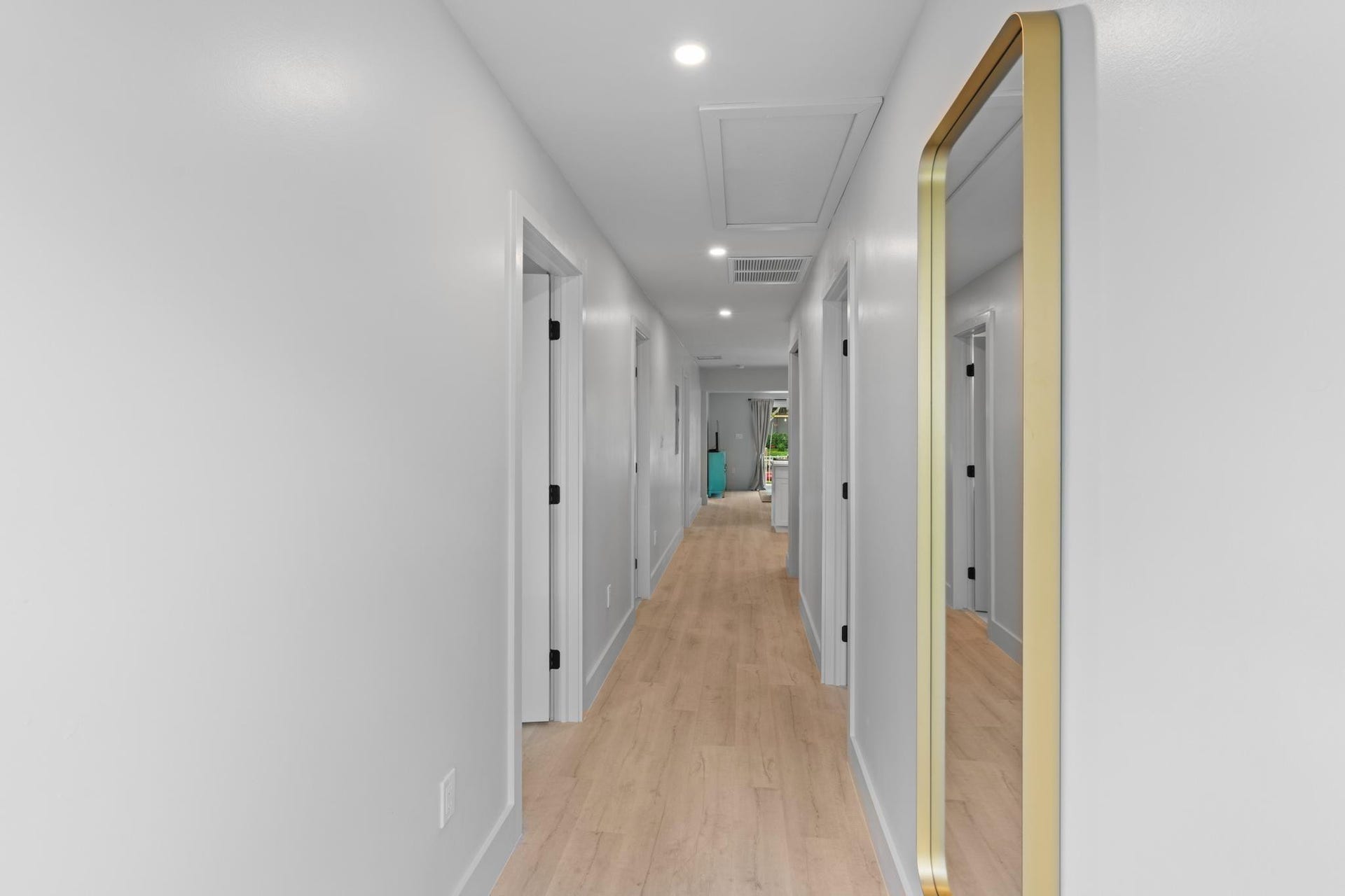 Recessed lighting illuminates wood-finish flooring in this hallway with white walls