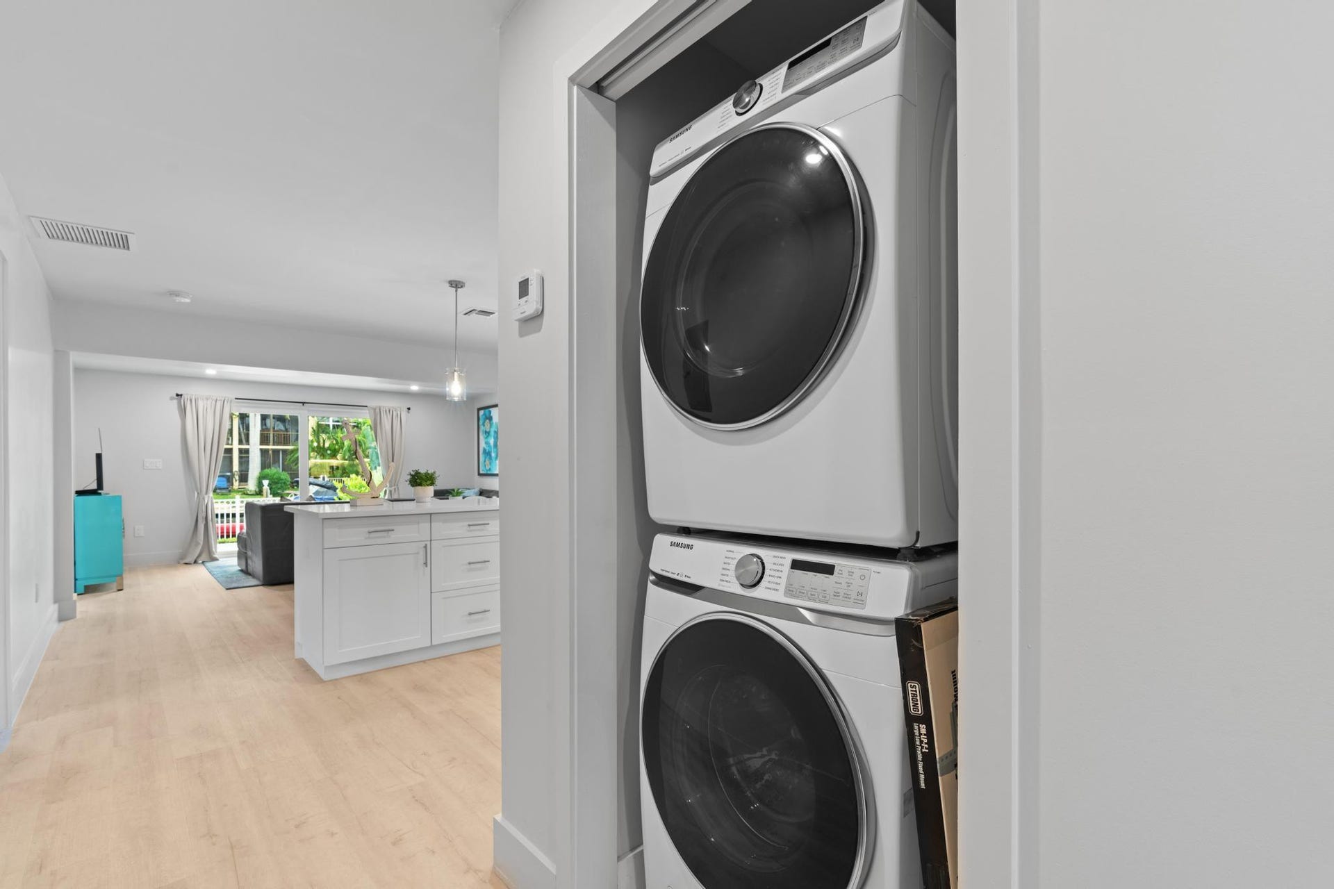 Stackable washer and dryer, light wood-finish flooring, white kitchen island with cabinetry, sliding glass doors, and recessed lighting